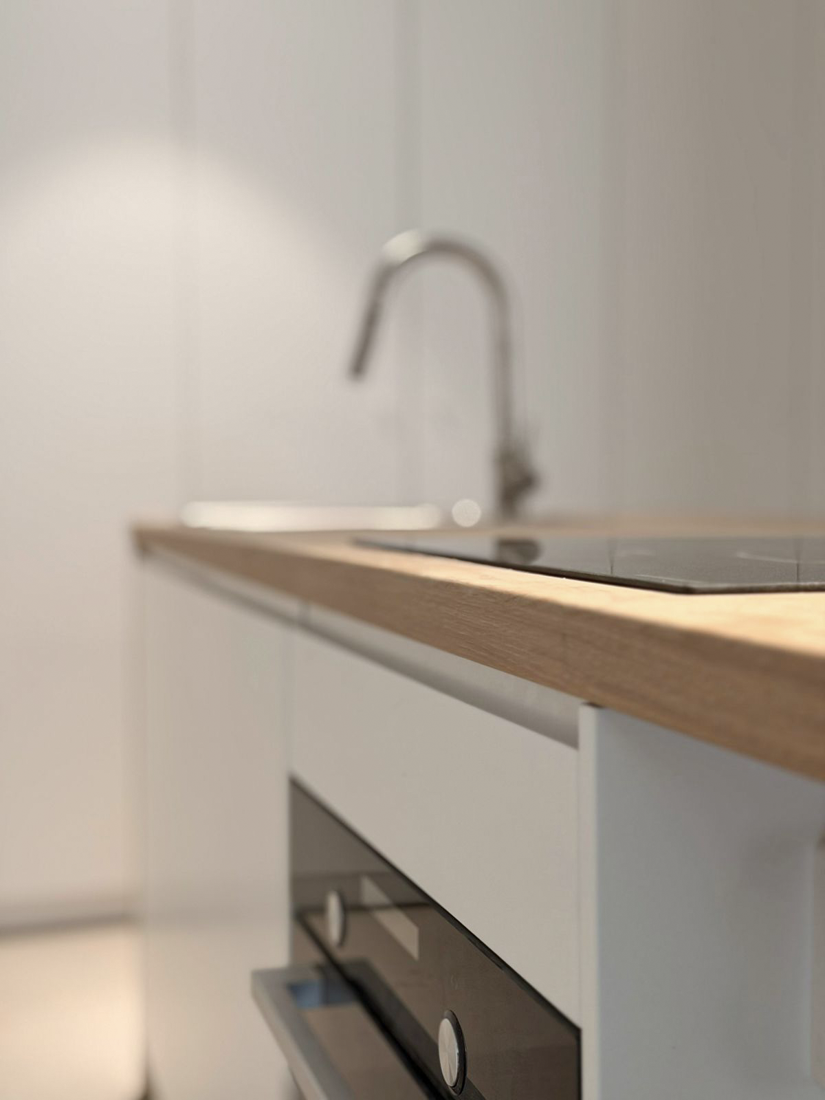 Close-up of kitchen countertop with a built-in oven and a kitchen faucet in the background.