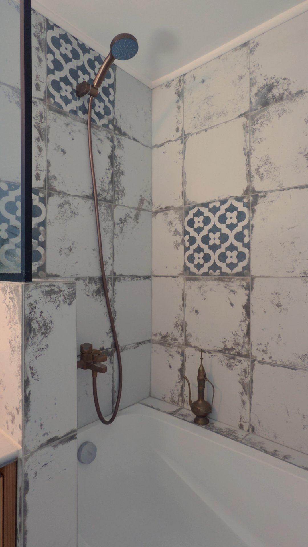 Shower with gray and white patterned tiled walls, brass fixtures, and a bronze showerhead.