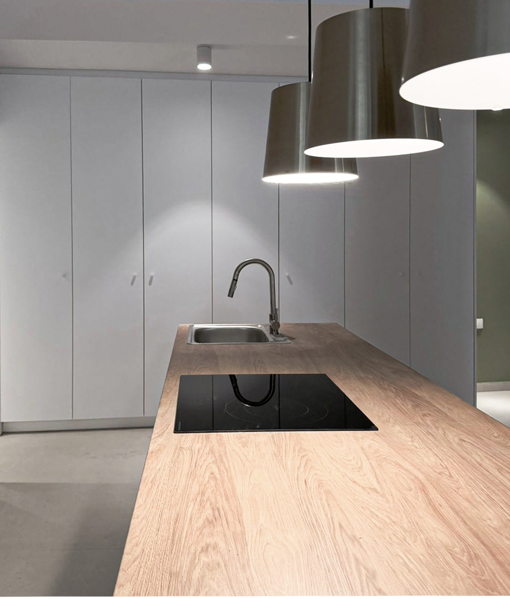Modern kitchen with a wooden countertop, black electric stove, stainless steel sink, and large metallic pendant lights hanging above.