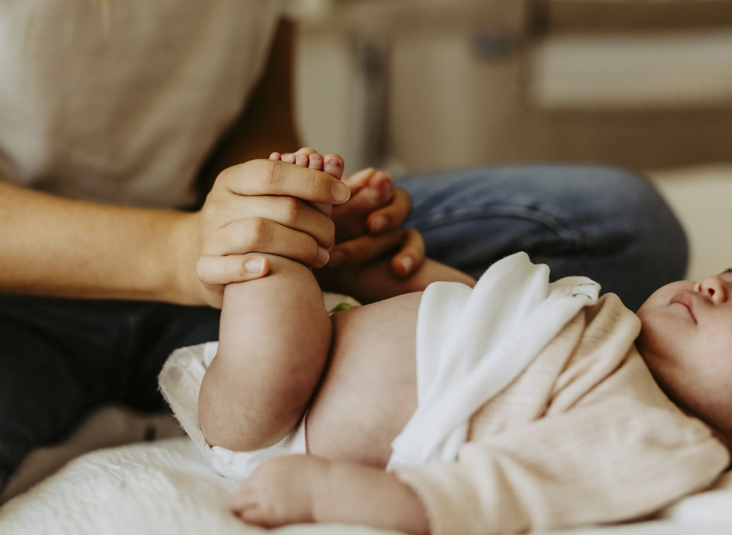 Nahaufnahme einer Hand, die eine Babyhand hält, während ein Baby auf dem Bauch liegt.