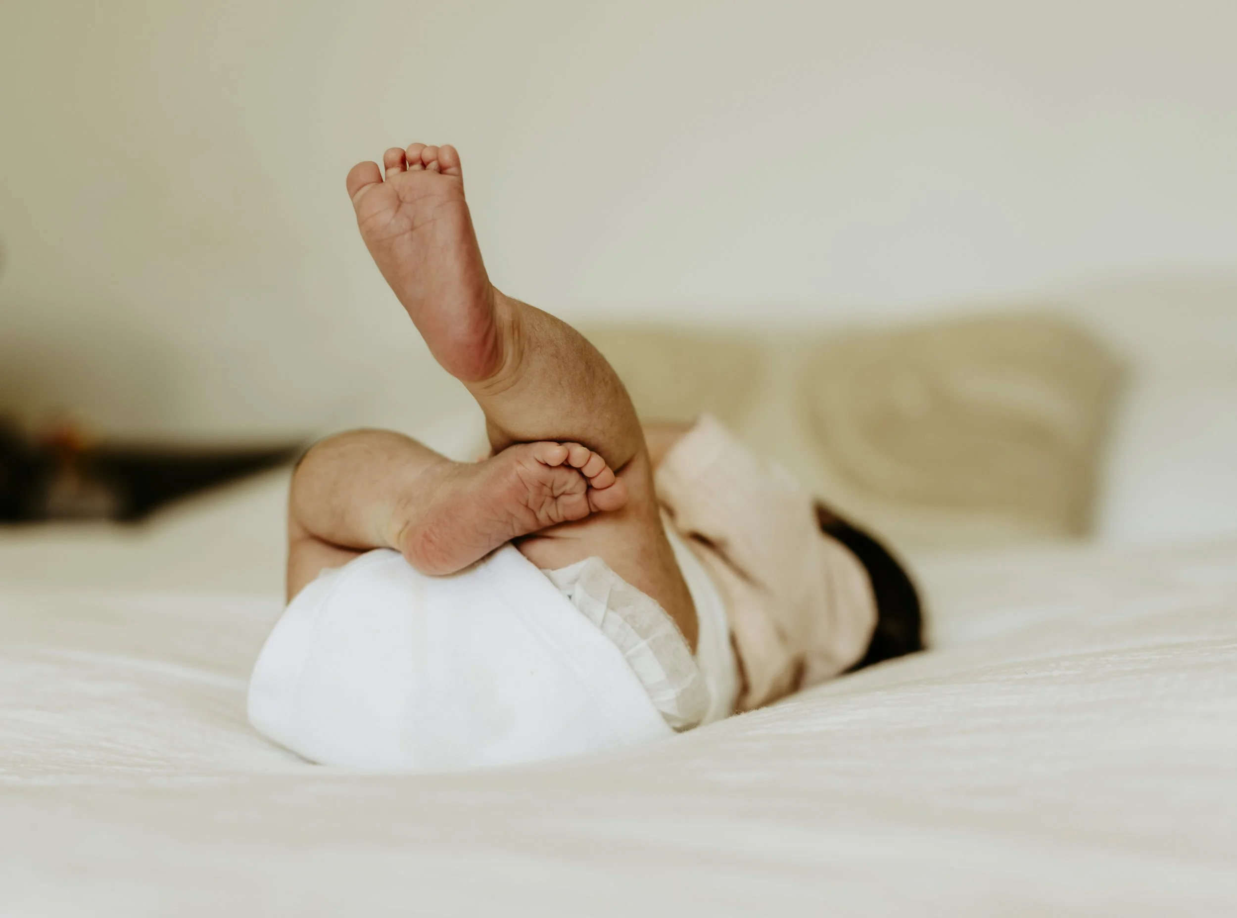 Nahaufnahme eines Babys, das auf seinem Bauch liegt und die Fäuste ballt, mit einem hellen, neutralen Hintergrund.