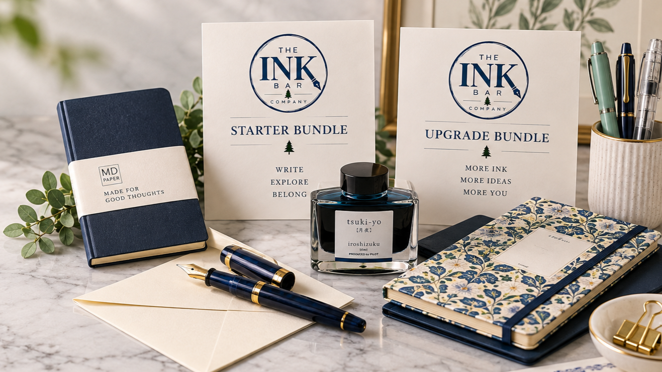 A collection of stationery items including a fountain pen, an ink bottle labeled 'tsuki-yo', notebooks, and informational signs about ink bundles on a marble surface.
