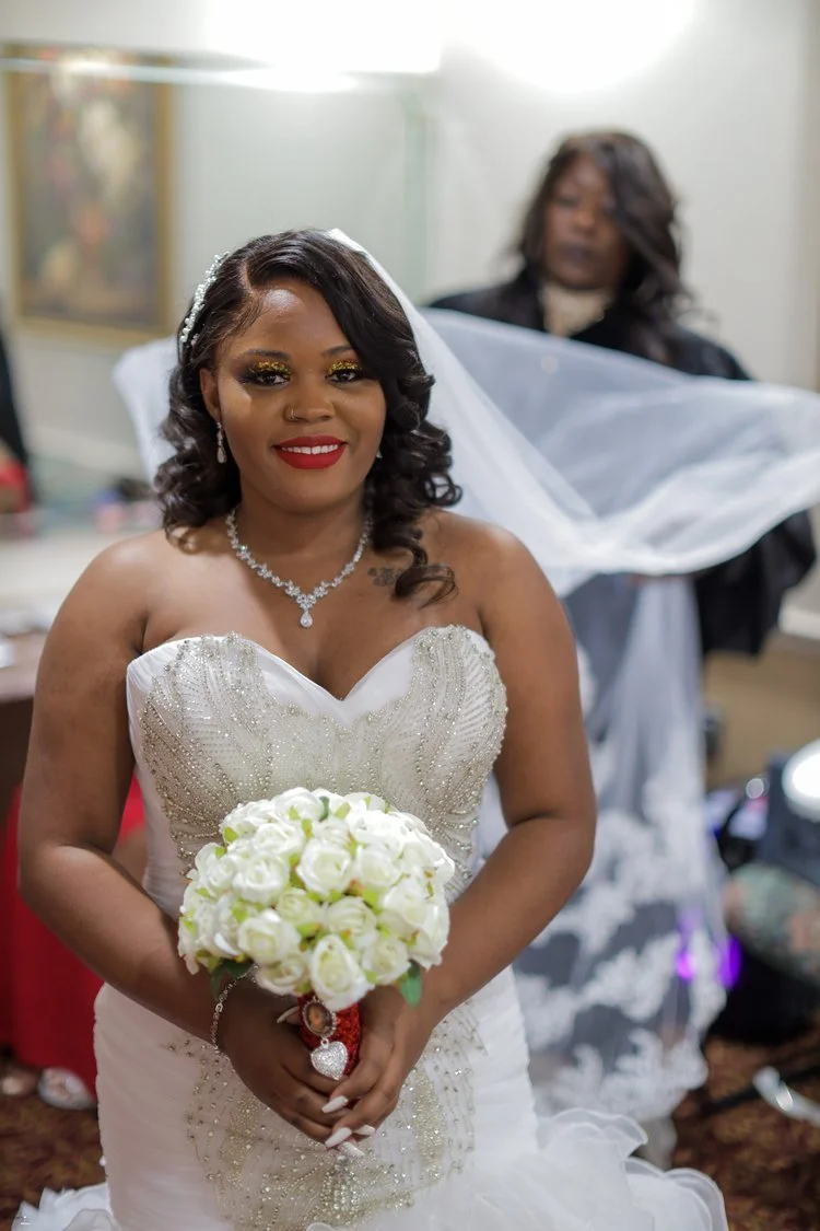 A bride in a white wedding dress with beaded details, holding a bouquet of white roses, and wearing jewelry including a necklace, earrings, and a bracelet.