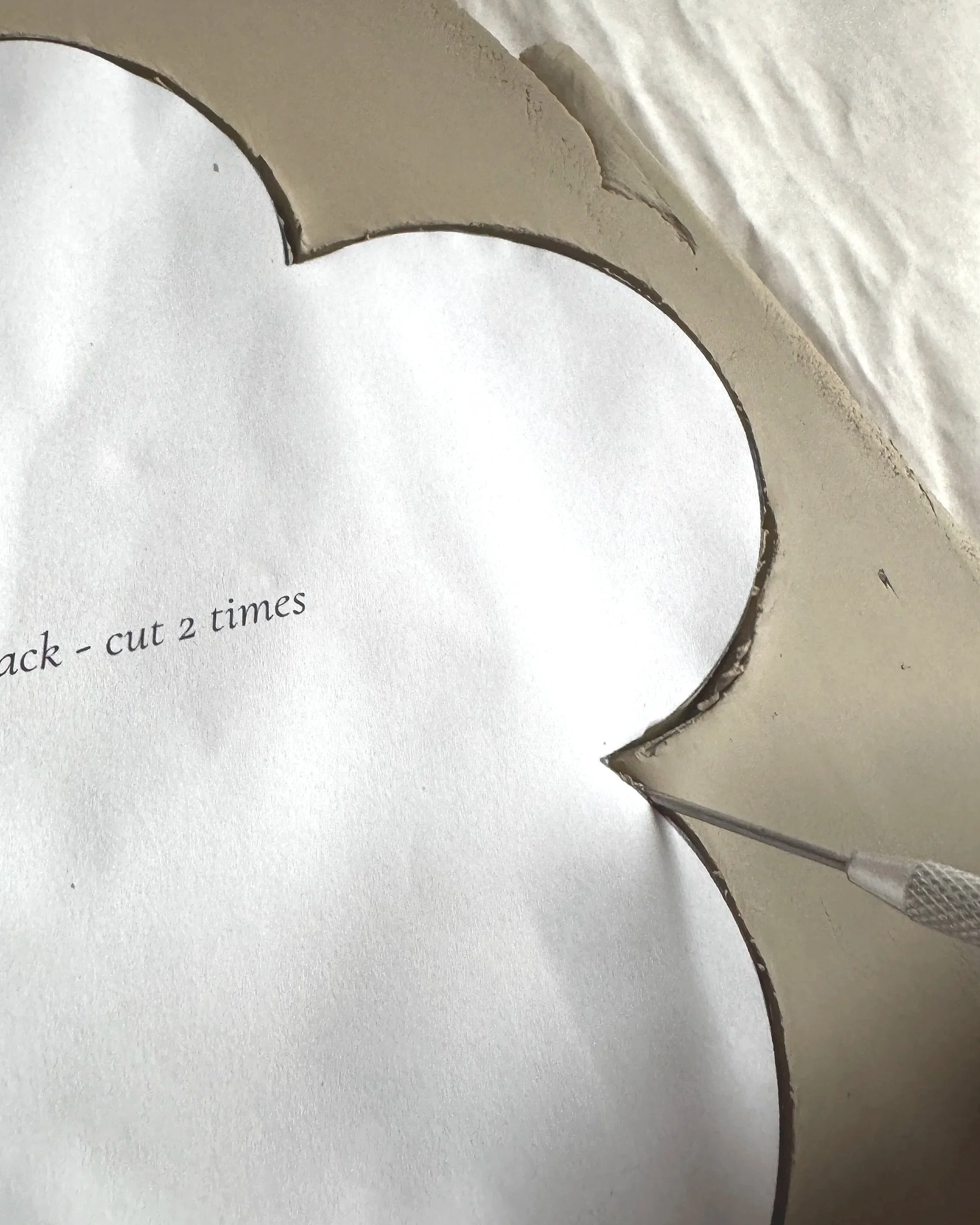 Nahaufnahme eines silbernen Papierschirms mit gewelltem Rand von THALIE DÉCO, über einem beschrifteten weißen Blatt Papier.