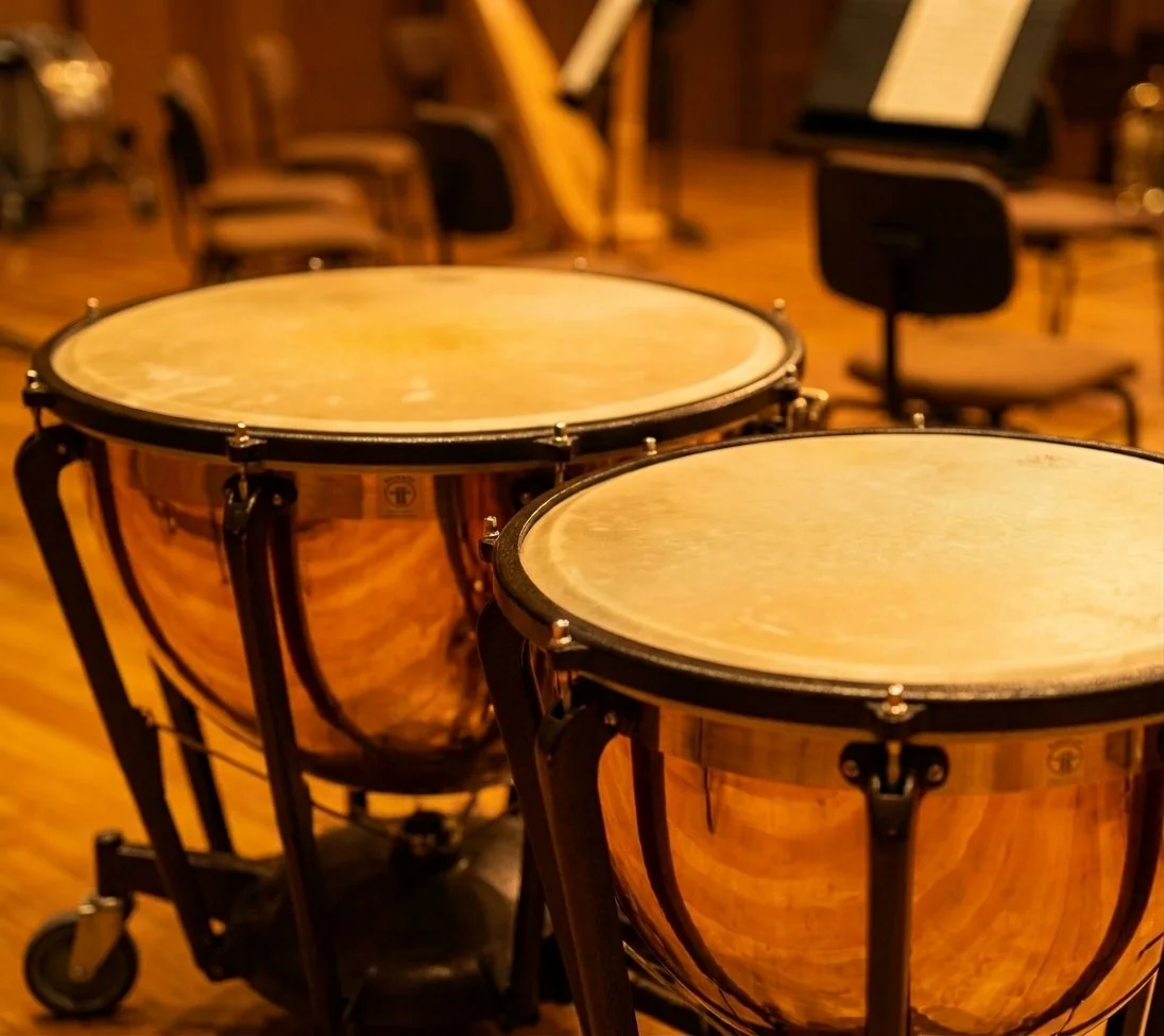 Two timpani drums in a music studio with chairs and sheet music stands in the background.