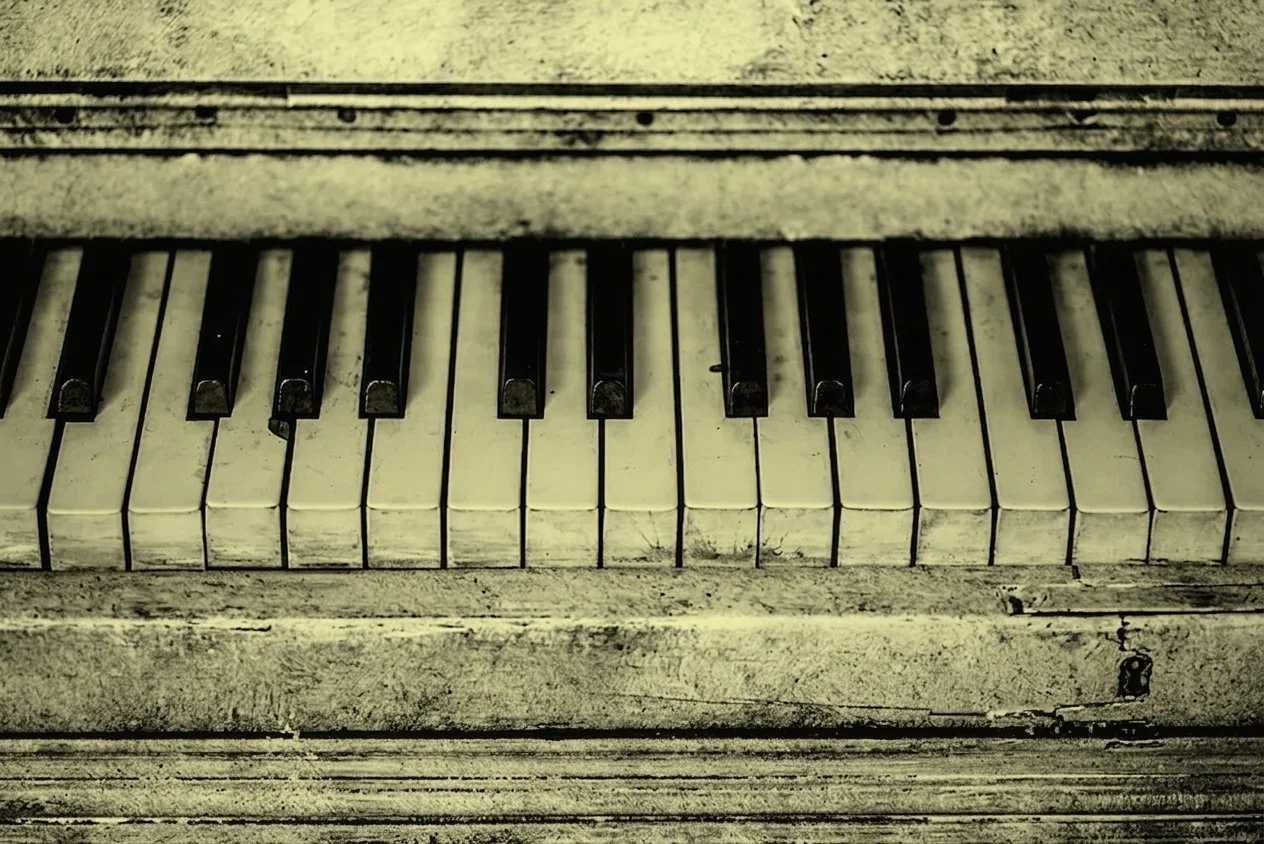 Close-up of old, dusty piano keys, with worn white and black keys, in an aged, weathered wooden case.