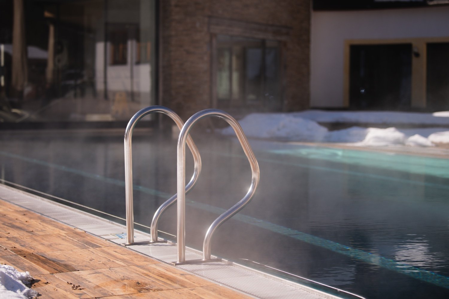 Schwimmbad mit Metallleiter, Holzdeck und Schneeflächen im Hintergrund.
