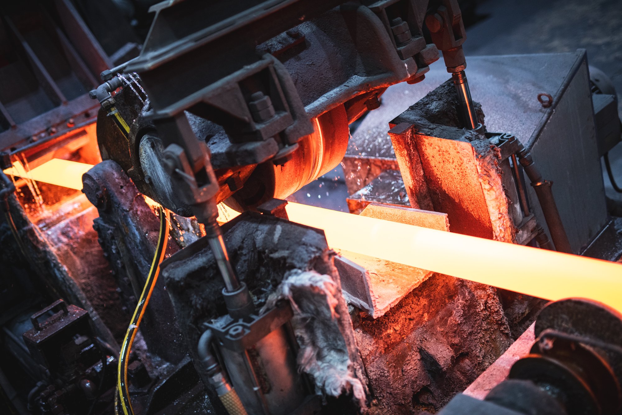 Ein Industrieofen erhitzt ein glühendes Metallstück, das auf einer feuerfesten Oberfläche liegt, umgeben von technischen Komponenten und Kabeln.