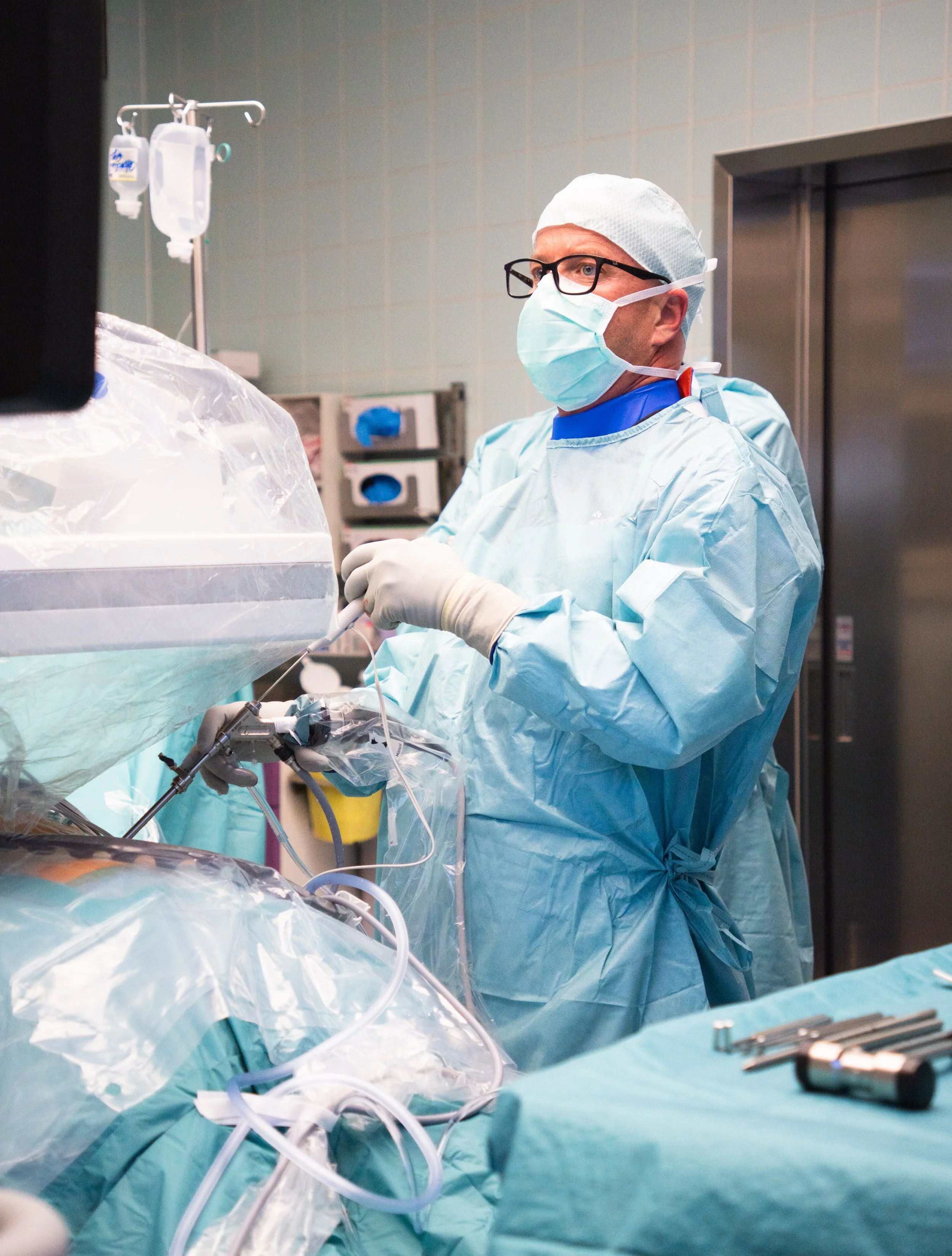 Ein Arzt in Operationskleidung, Maske und Brille führt eine Operation im Operationssaal durch.