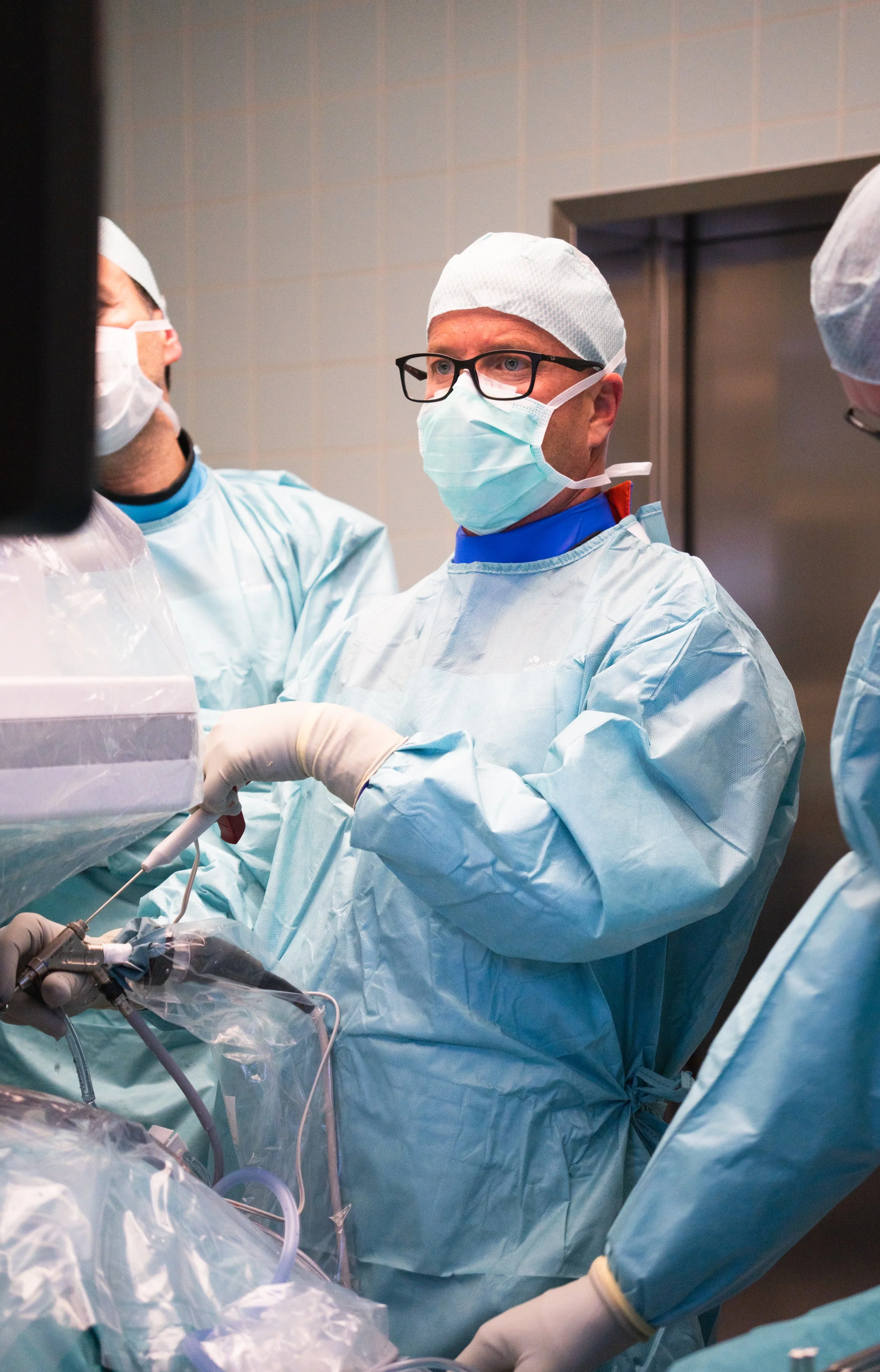 Team von Chirurgen während einer Operation im Operationssaal, alle tragen Schutzkittel, Masken, Hauben und Brillen.