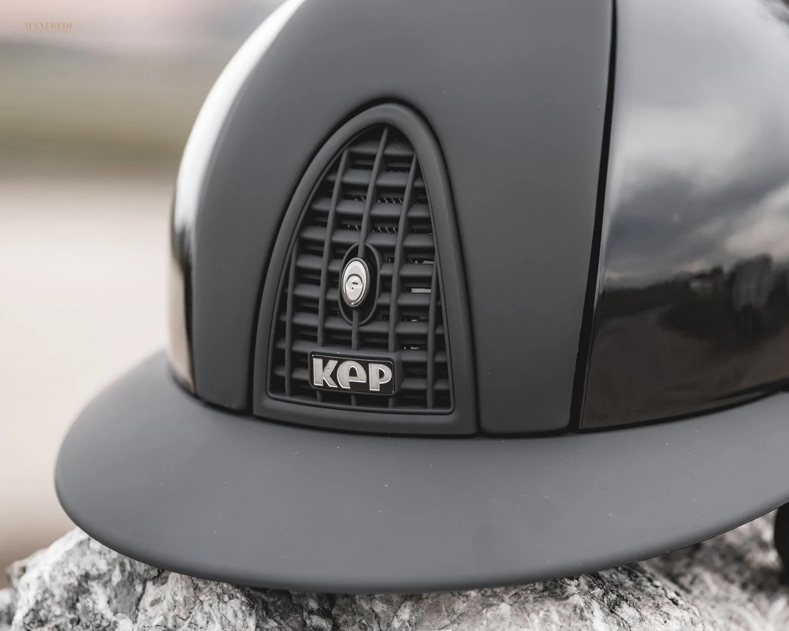 Nahaufnahme eines schwarzen Autoventils mit dem Logo 'KAP' auf der Front, montiert auf eine dunkle Lackoberfläche, sitzend auf einem grauen, strukturierten Steinboden.
