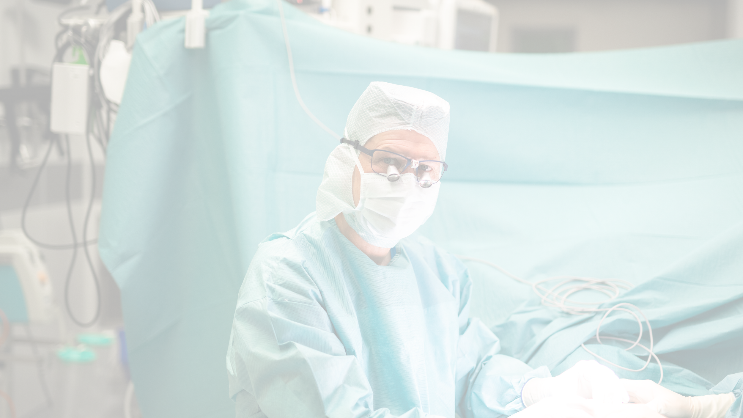 Ein Chirurg trägt eine Schutzmaske, Operationsbrille und eine Haube während eines chirurgischen Eingriffs im Operationssaal.