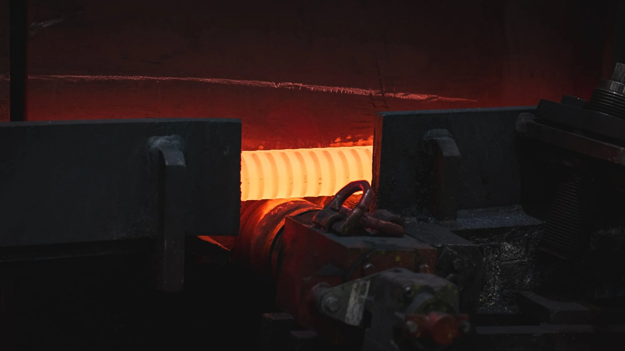 Sehr heißer Metallblock in einem Industrieofen, der rot leuchtet, umformung oder Gießen sichtbar, mit metallischen Werkzeugen und Zubehör.