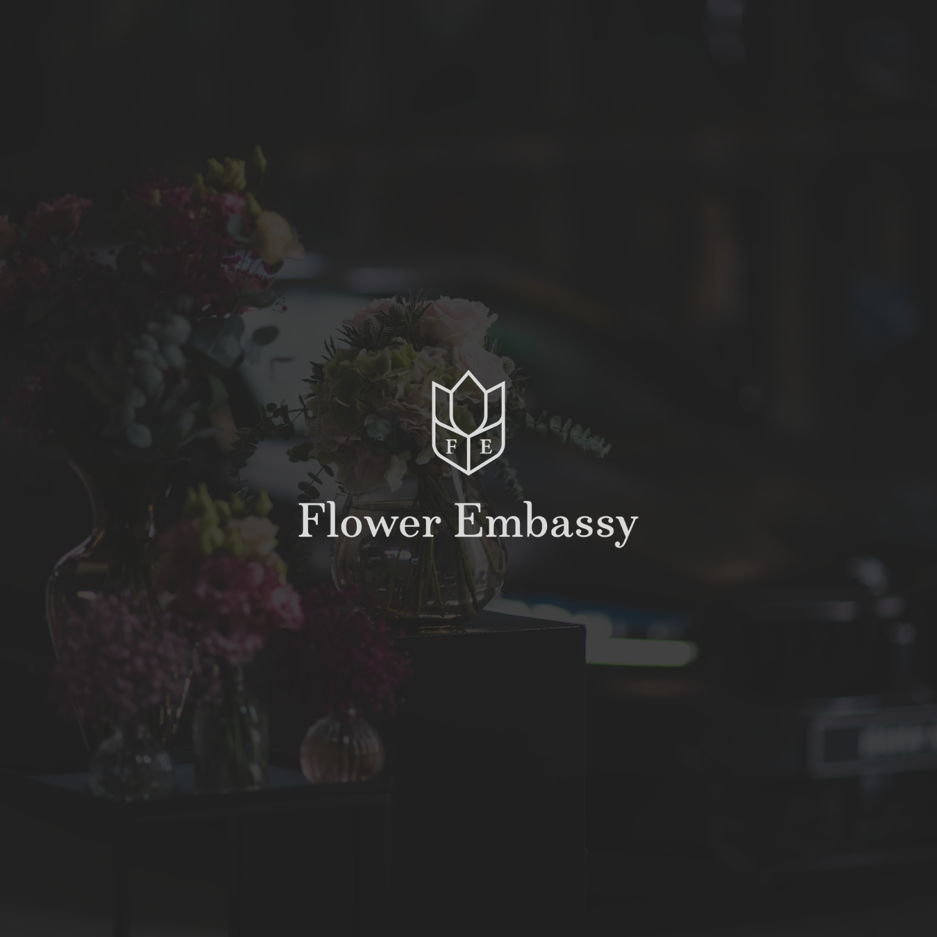 Logo von der 'Flower Embassy' auf einer dunklen Hintergrund mit Blumenvasen