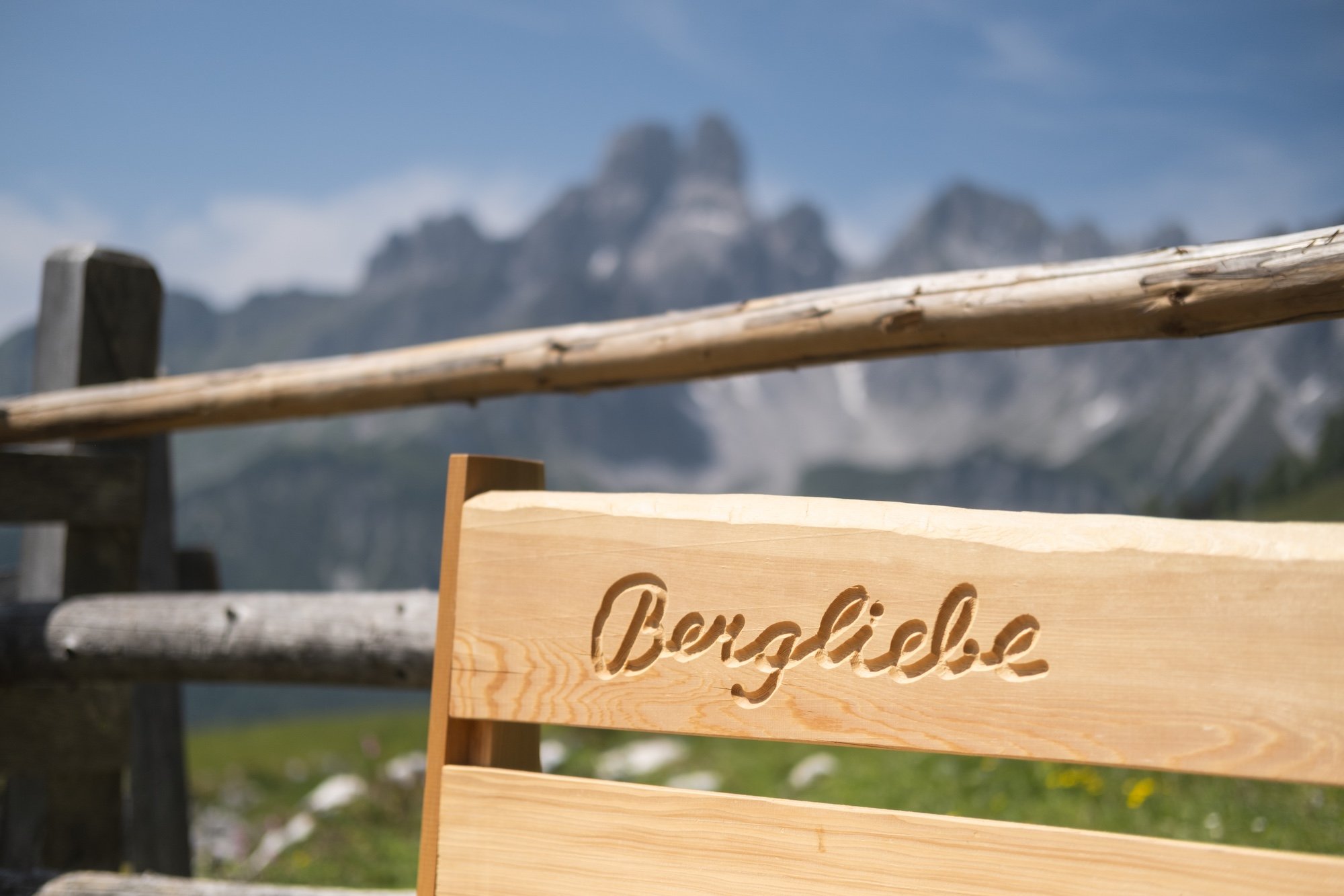 Holzschild mit dem Schriftzug "Bergisel" vor einer Berglandschaft mit Bergen im Hintergrund, blaue Himmel mit Wolken.