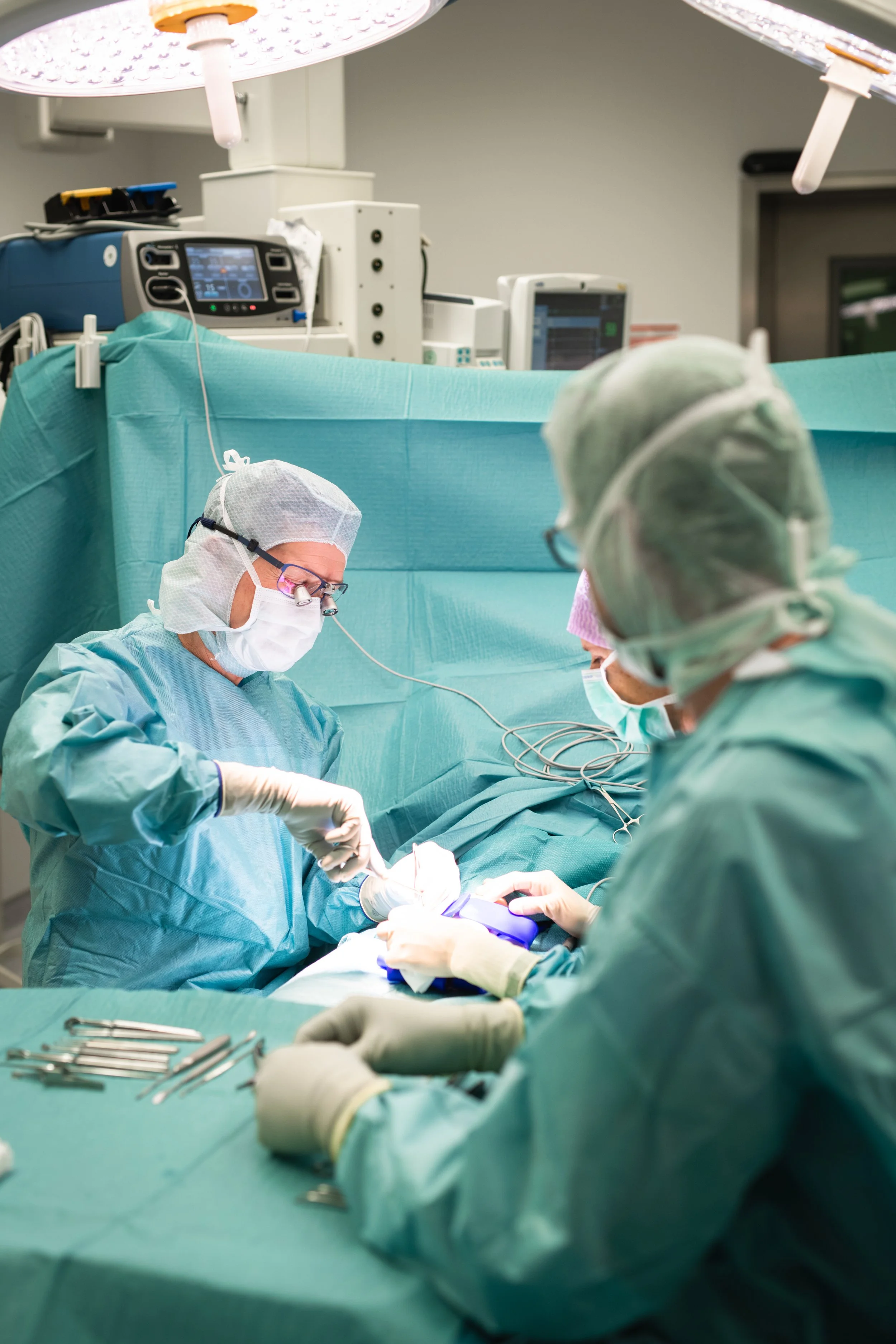 Ärzte und OP-Personal bei einer Operation in einem Operationssaal, medizinische Geräte und chirurgische Instrumente sichtbar.