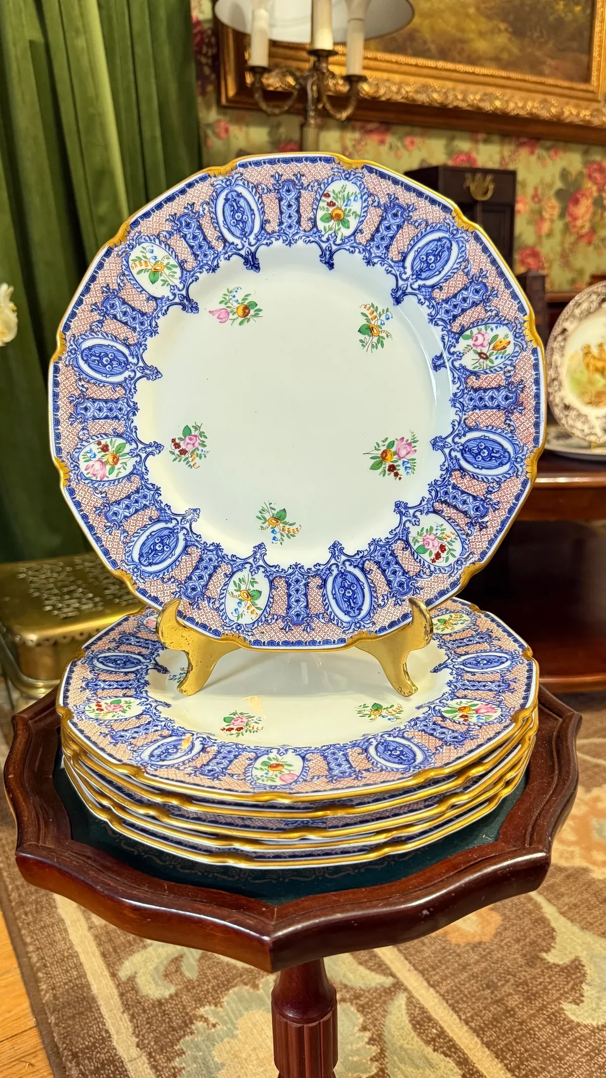 Stack of decorative porcelain plates with a blue and floral pattern, displayed on a wooden stand in an ornate room.