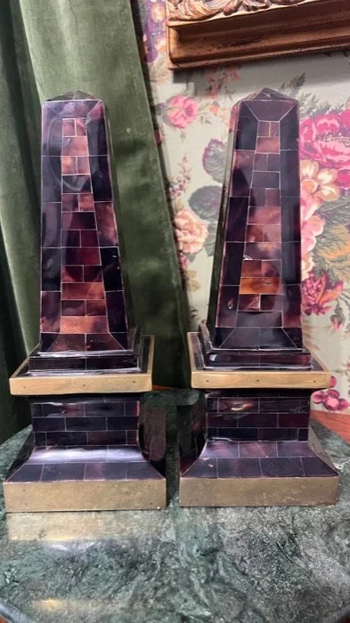 Two matching vintage-style lamps with dark tiled bases and taller, pyramid-shaped tops, sitting on a green marble surface in front of a floral wallpaper.