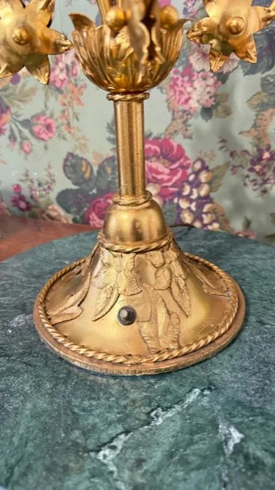 Close-up of a vintage gold-colored candle holder with ornate floral details, placed on a green marble surface.