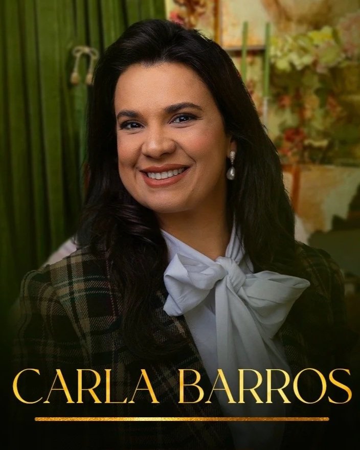 Photograph of Carla Barros smiling, wearing pearl earrings, a white blouse with a bow, and a plaid blazer, with a decorated background.