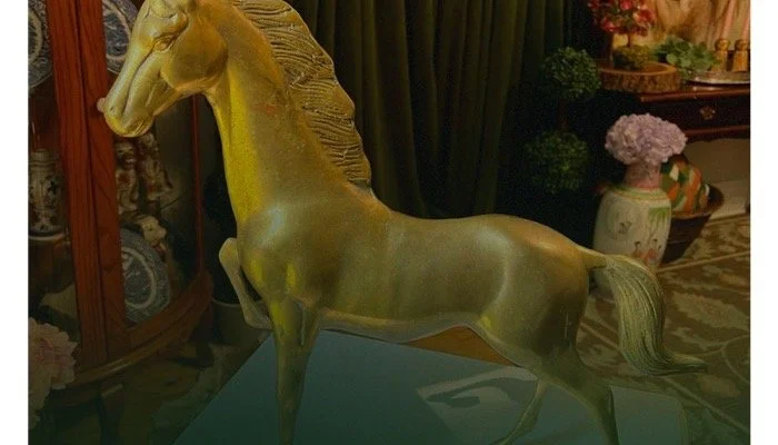 A golden horse sculpture on a blue table in a living room, with flowers and furniture in the background.