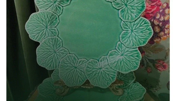 Decorative table set with a large round glass top and a gold-colored base, surrounded by green leaf-shaped placemats.