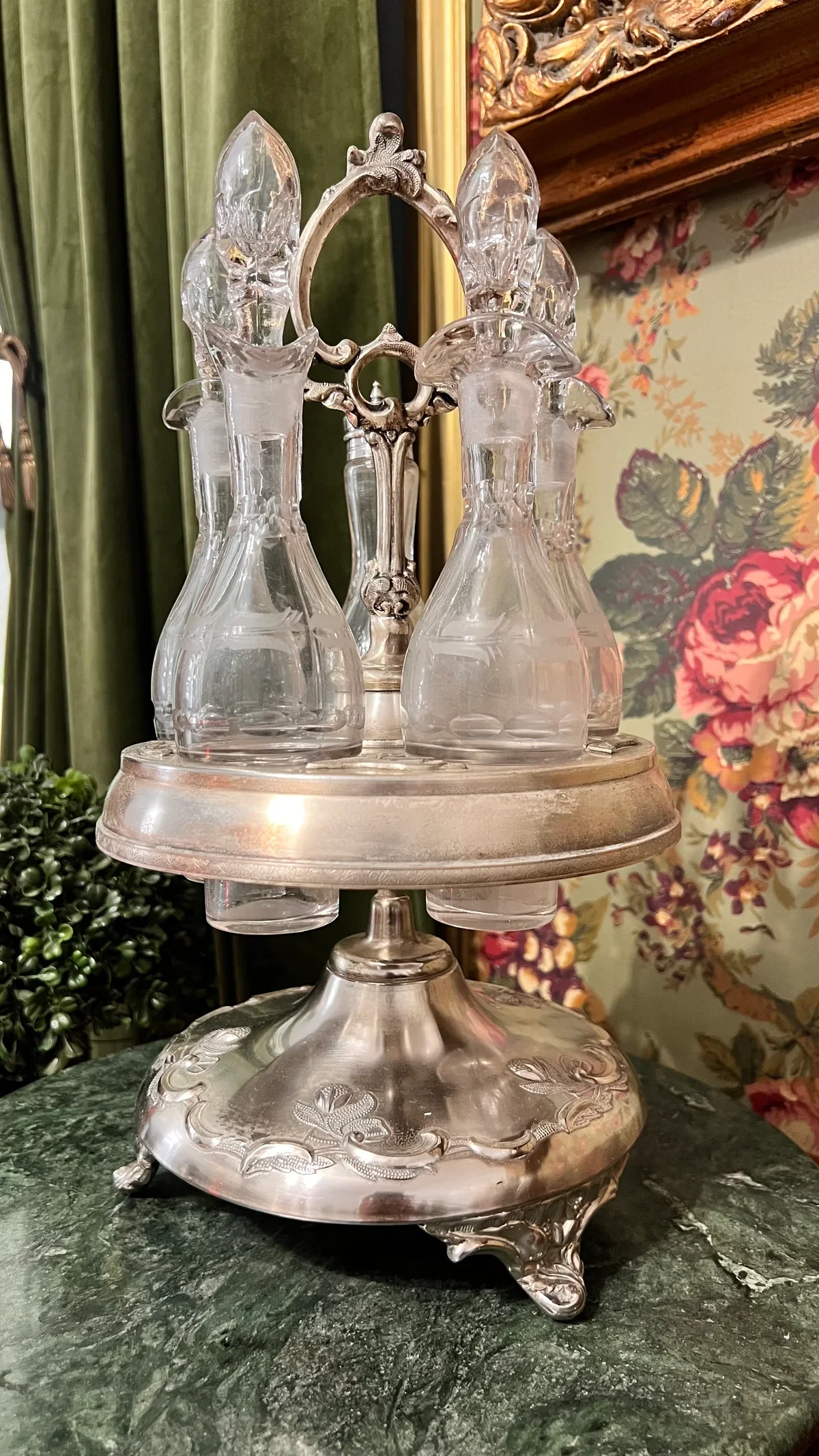 A vintage glass and metal candelabra holding four glass candle holders, set on a green marble surface with a floral wallpaper background.