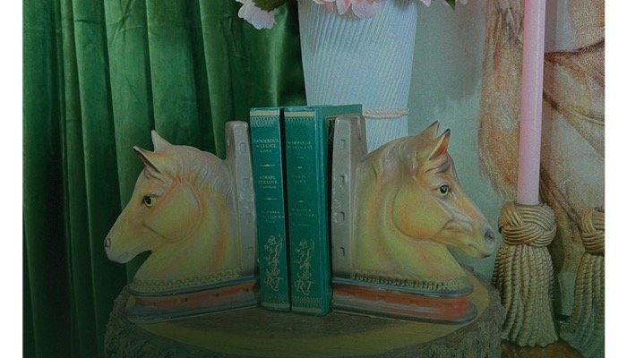 Two decorative horse head bookshelves with a few books between them, placed on a small table or shelf.