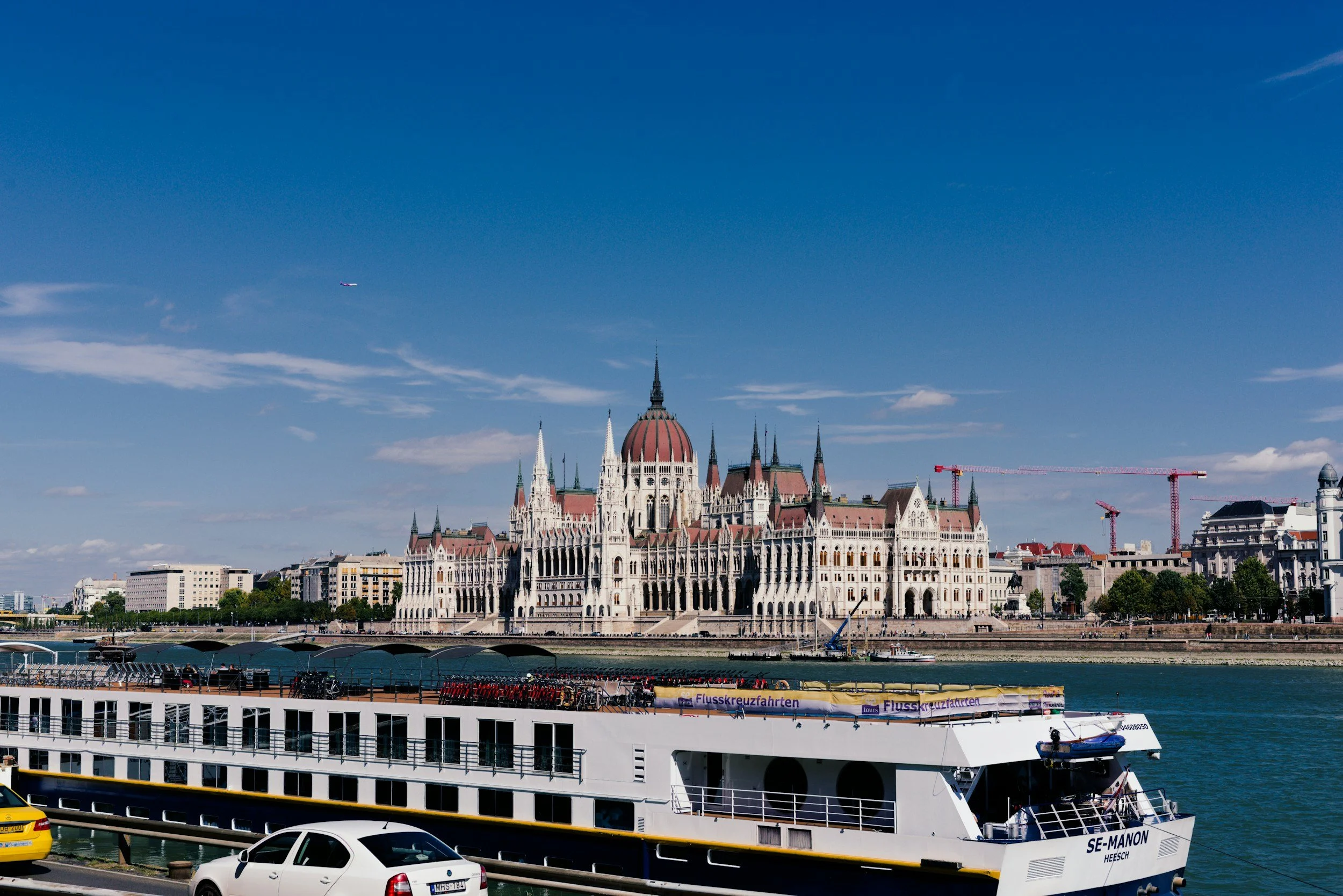 View of the Hungarian Parliament Building in Budapest with a cruise ship docked along the riverfront.