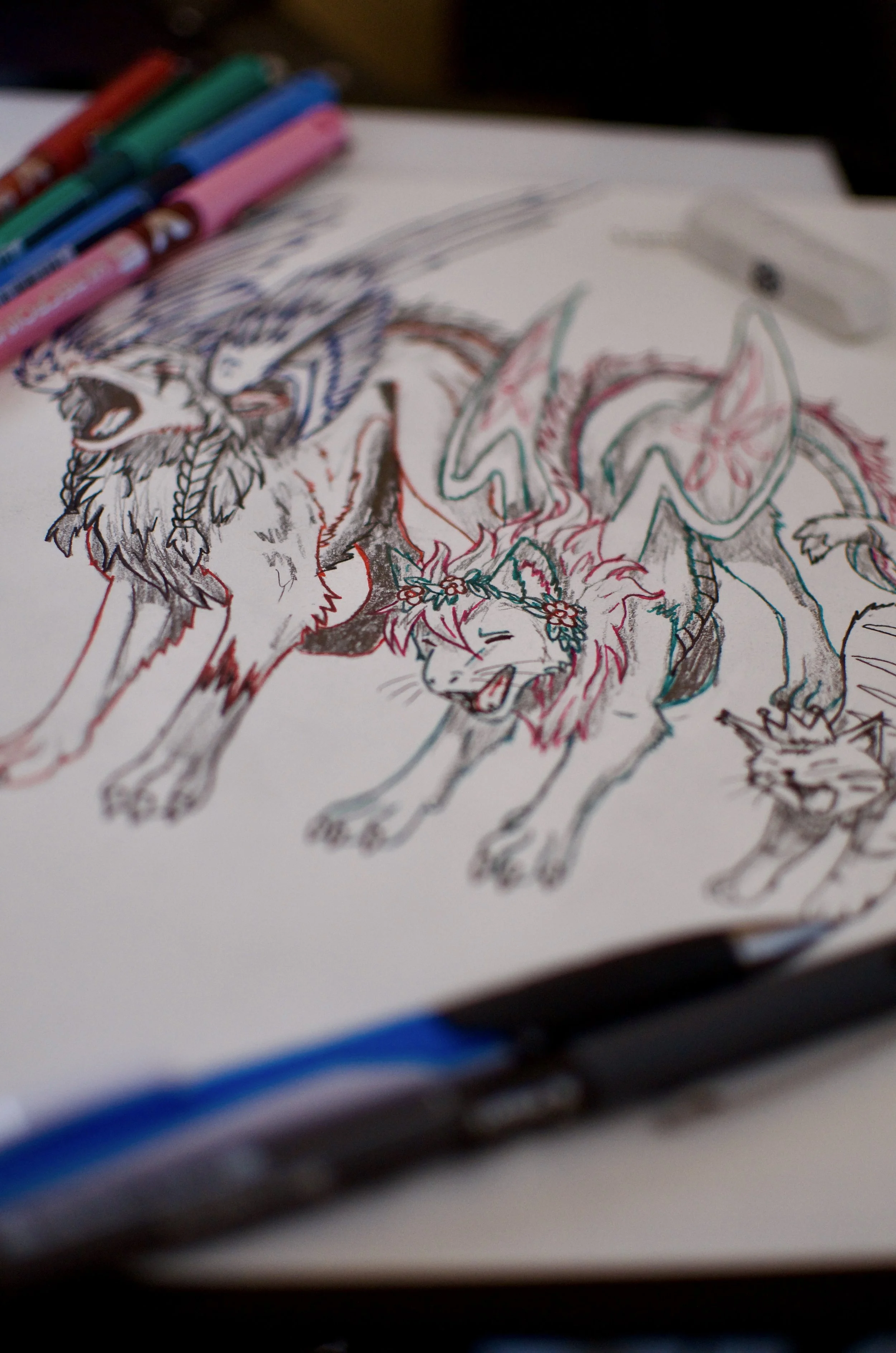 Colorful hand-drawn illustration of a wolf with a floral crown on its head, featuring vibrant colors and detailed linework, resting on a white sheet of paper.