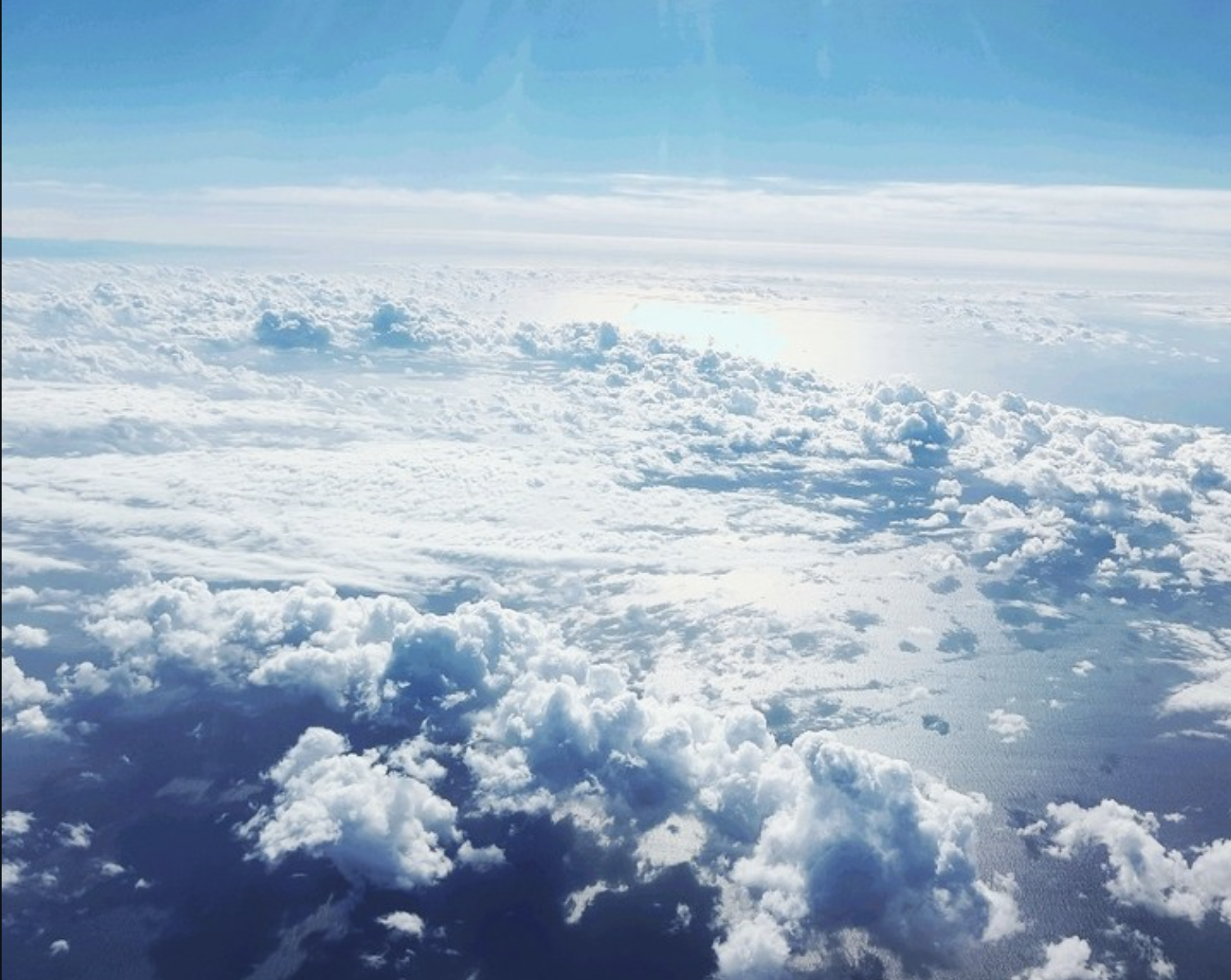 A view from above the clouds showing a vast expanse of white clouds with a hint of blue sky at the horizon.