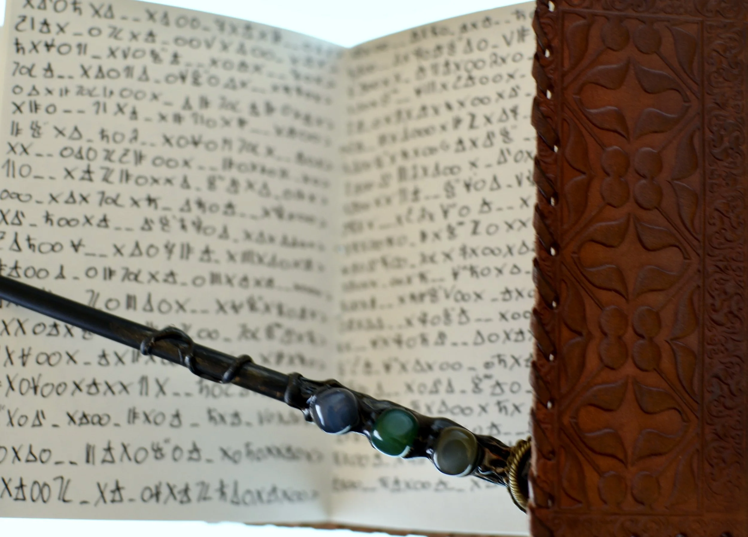 Close-up of an open book with code-like symbols, a carved leather wallet, and a beaded bracelet with black and green beads.