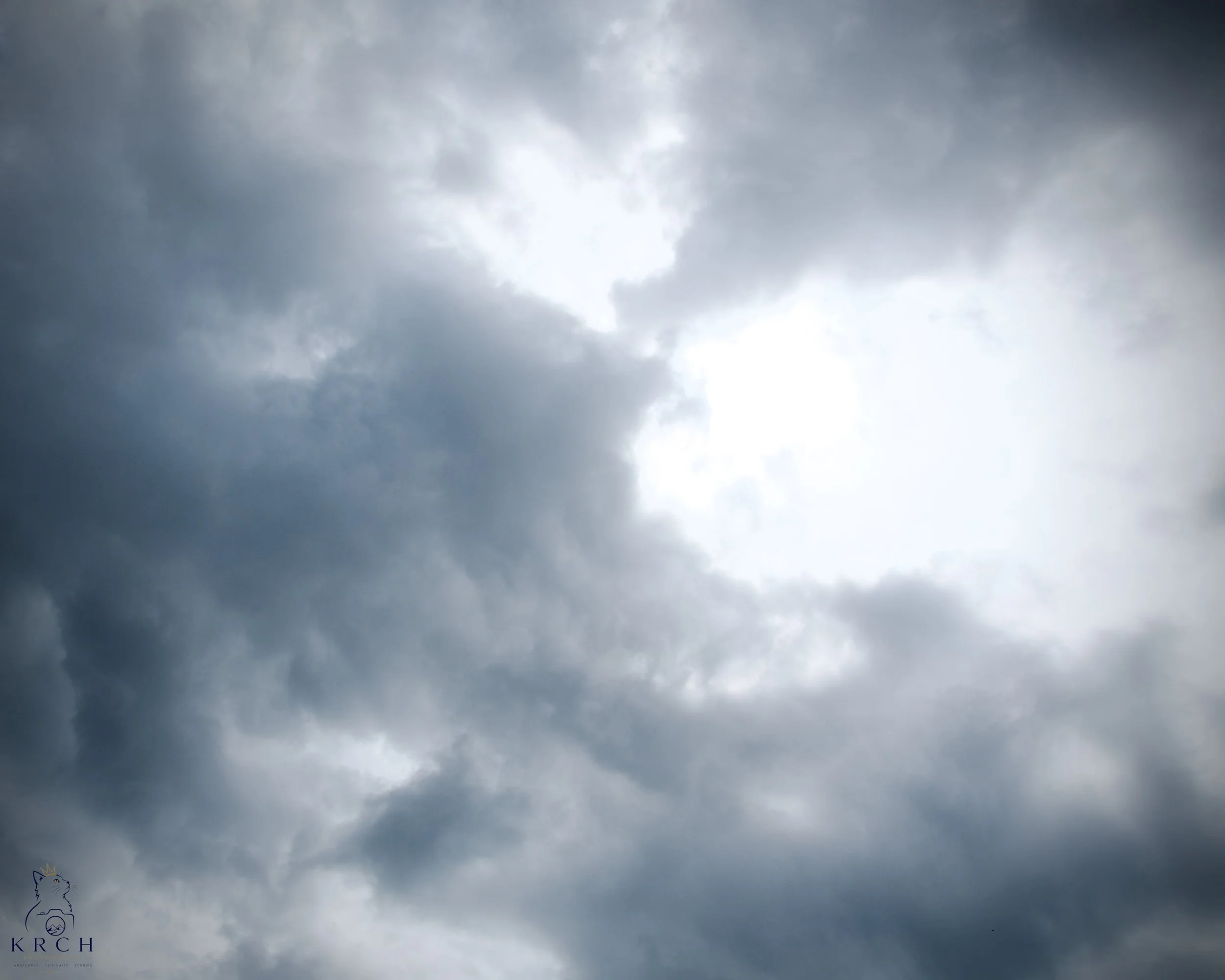 Upward view of a cloudy sky with dark clouds and bright sunlight breaking through.