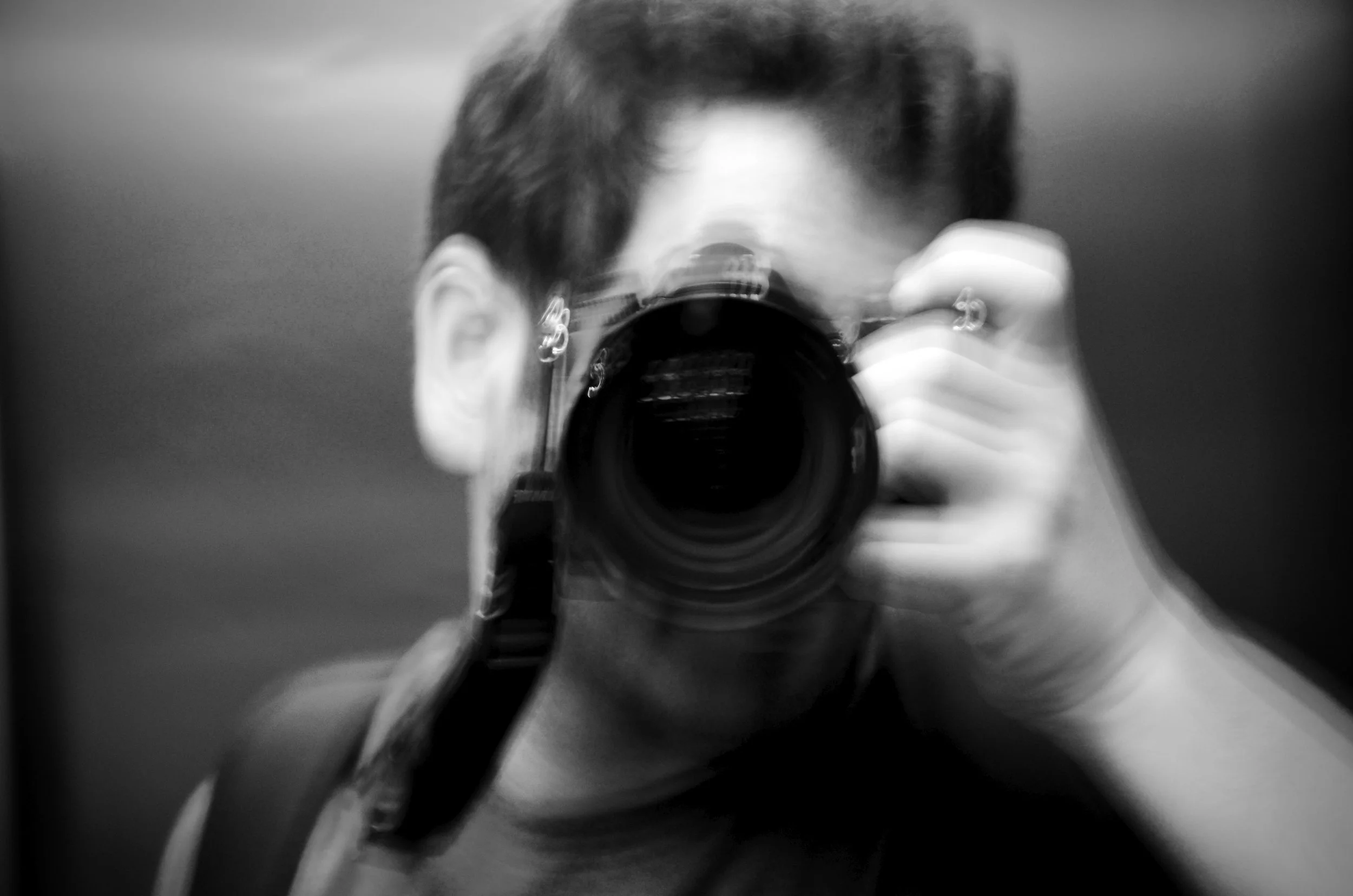 A person taking a mirror selfie with a camera, with short hair, in a monochrome setting.