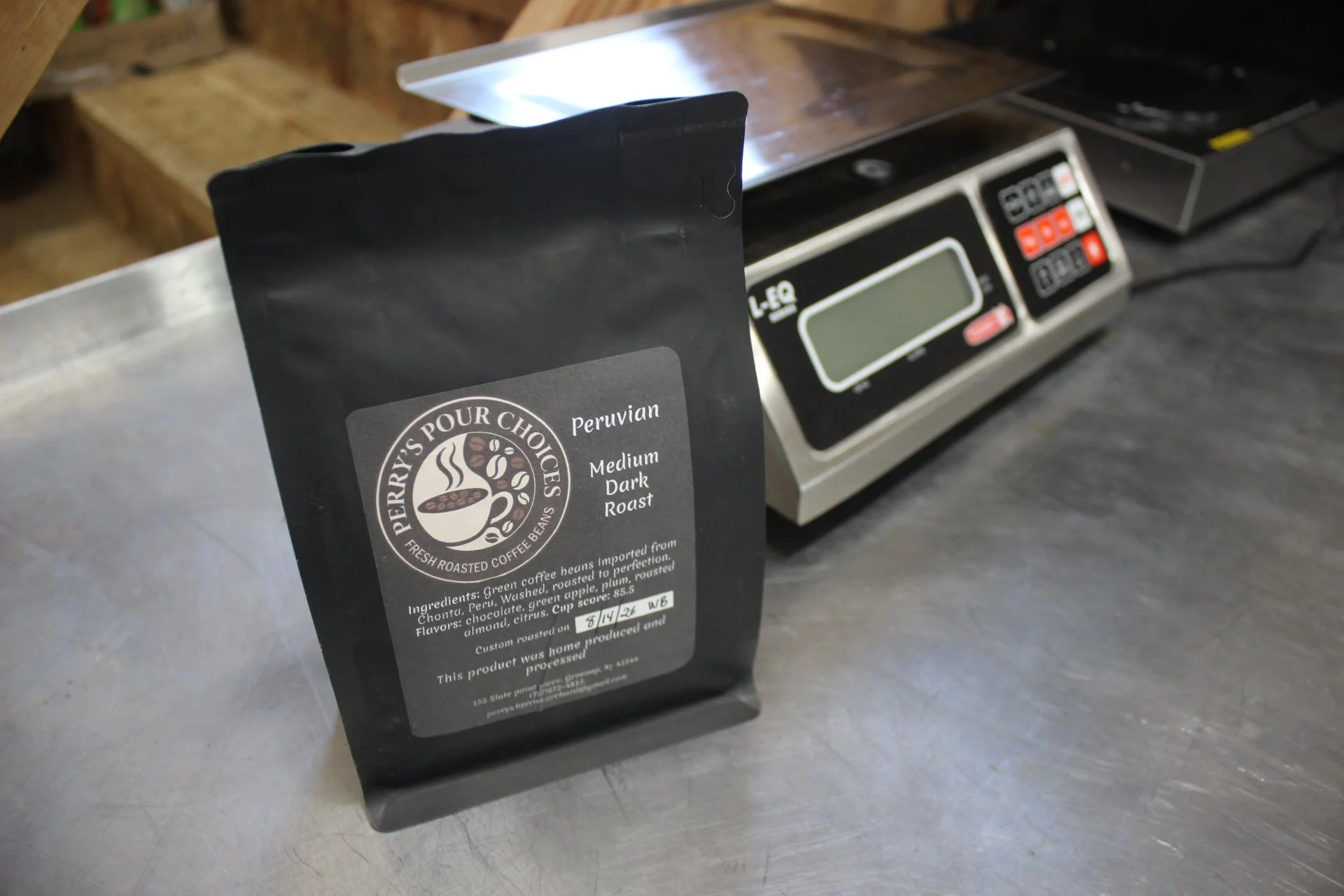 Package of Perrys Pour Choices Peruvian medium dark roast coffee beans on a stainless steel counter with a digital weighing scale in the background.