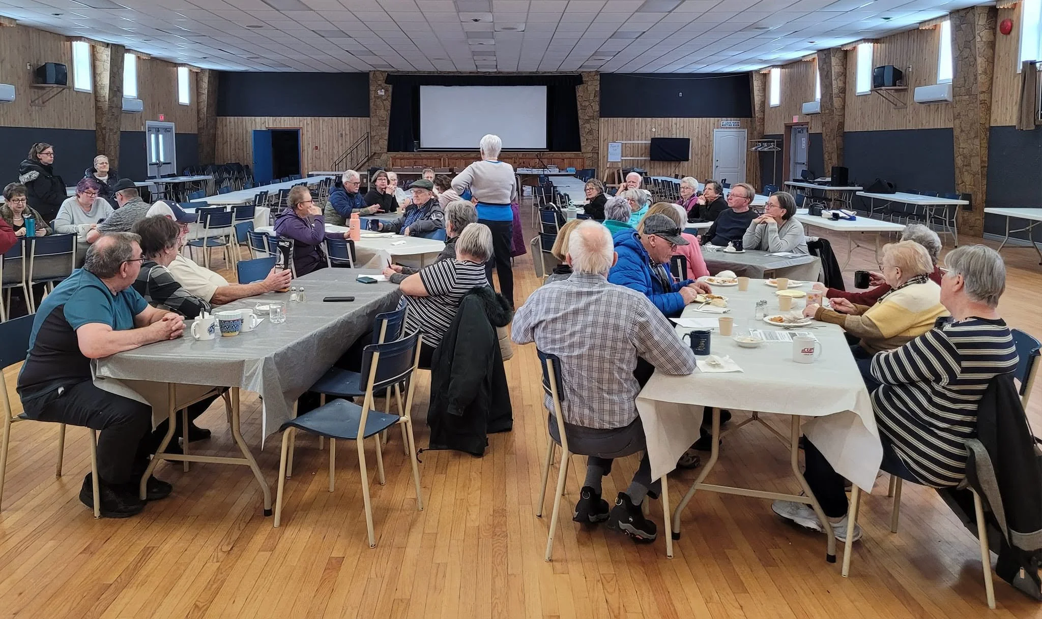 Seniors gathered around tables in a large community hall at a STAC meeting