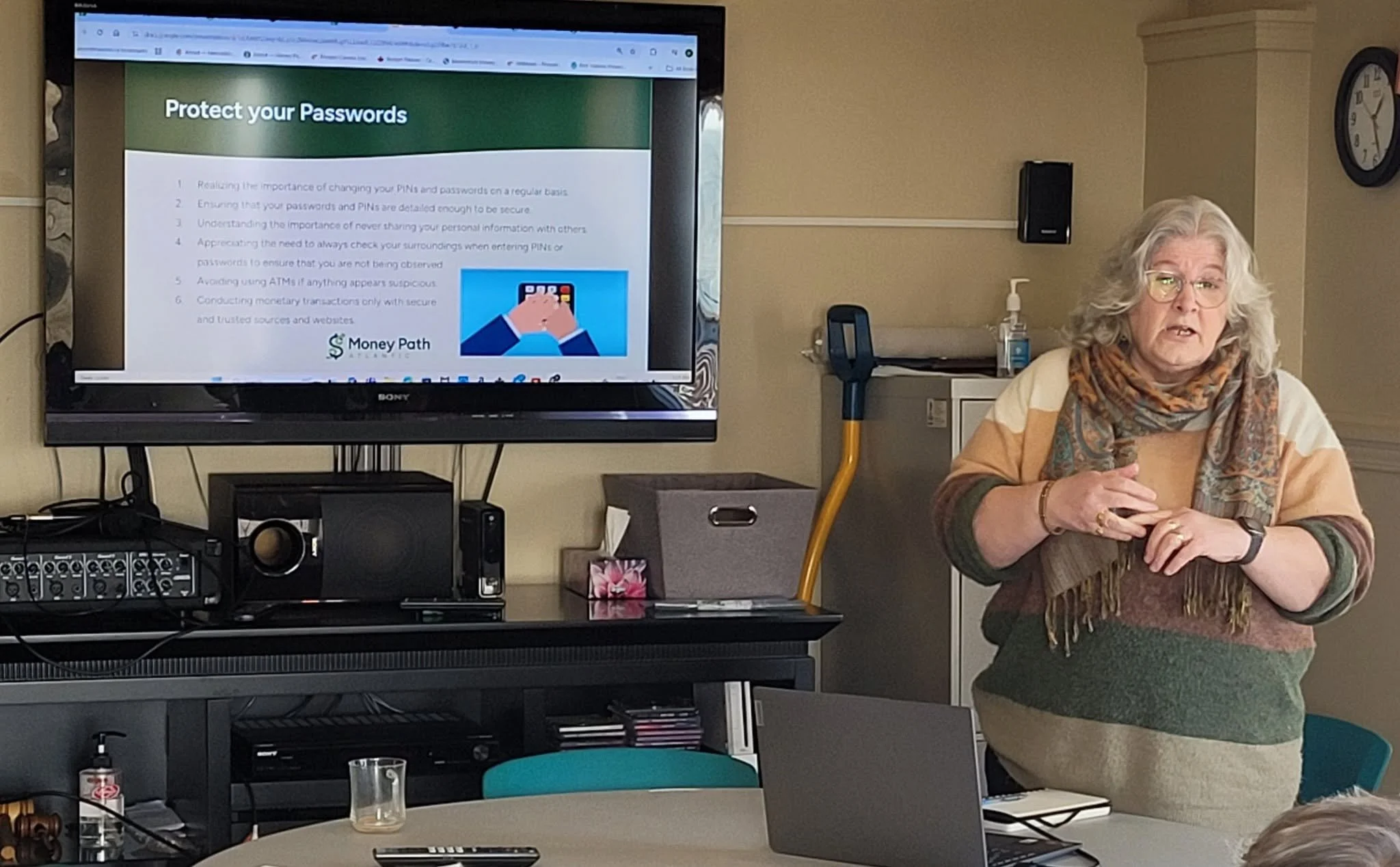Presenter speaking to seniors about protecting their passwords, with a slide on a TV screen