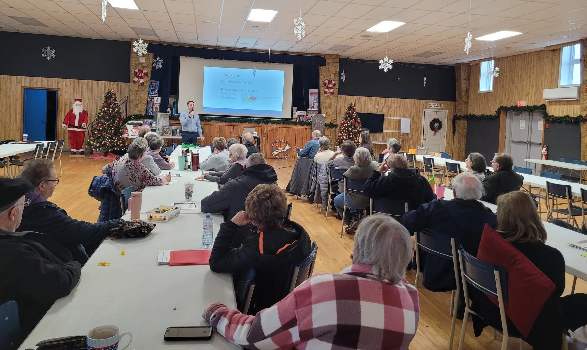 Crowd at a STAC holiday meeting in a decorated community hall, with a Christmas tree and Santa at the front