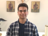 Young man standing indoors with two religious icons hanging on the wall behind him.