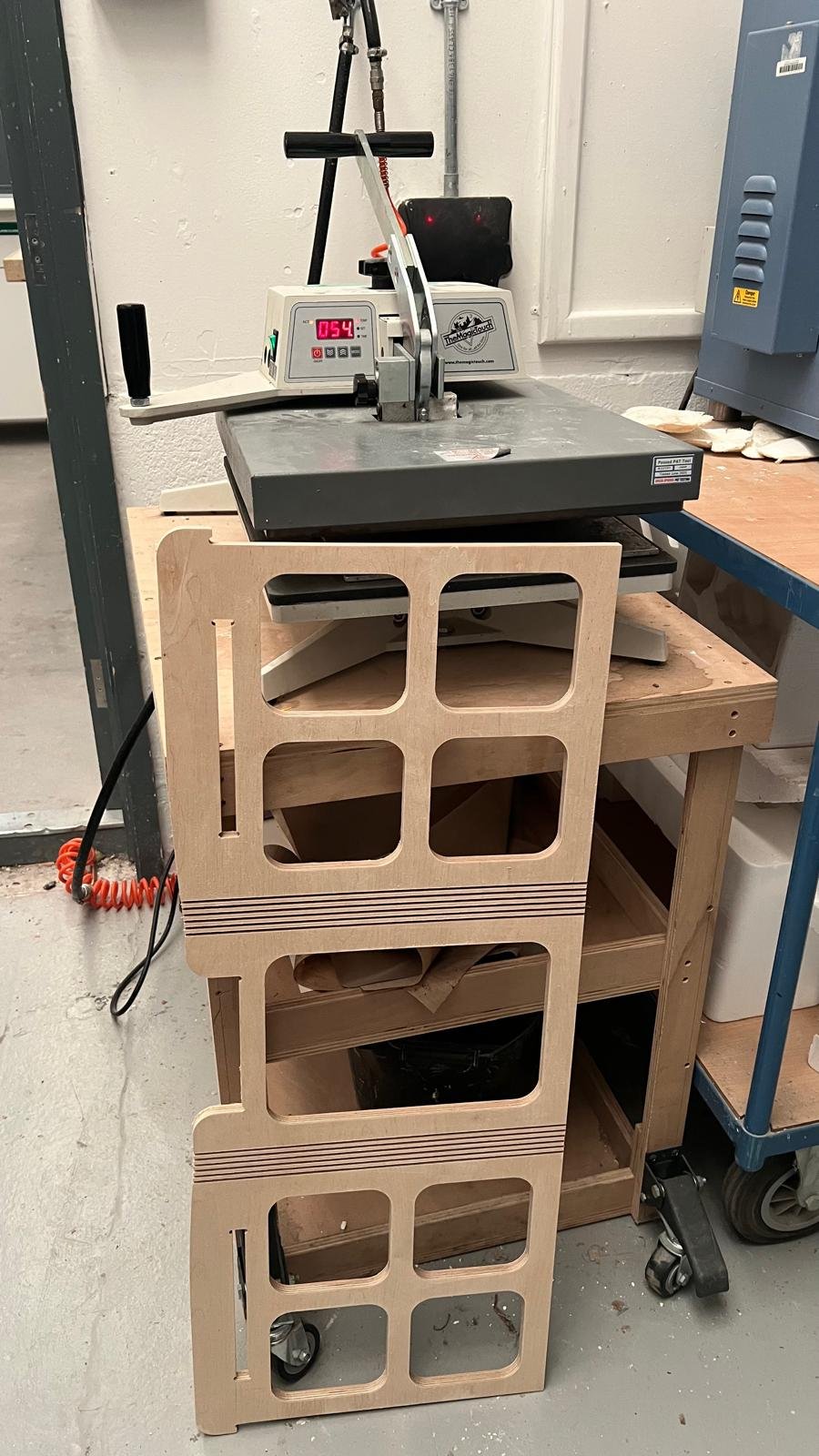 A laser cutting machine on a wooden workbench with a custom wooden template nearby in a workshop.