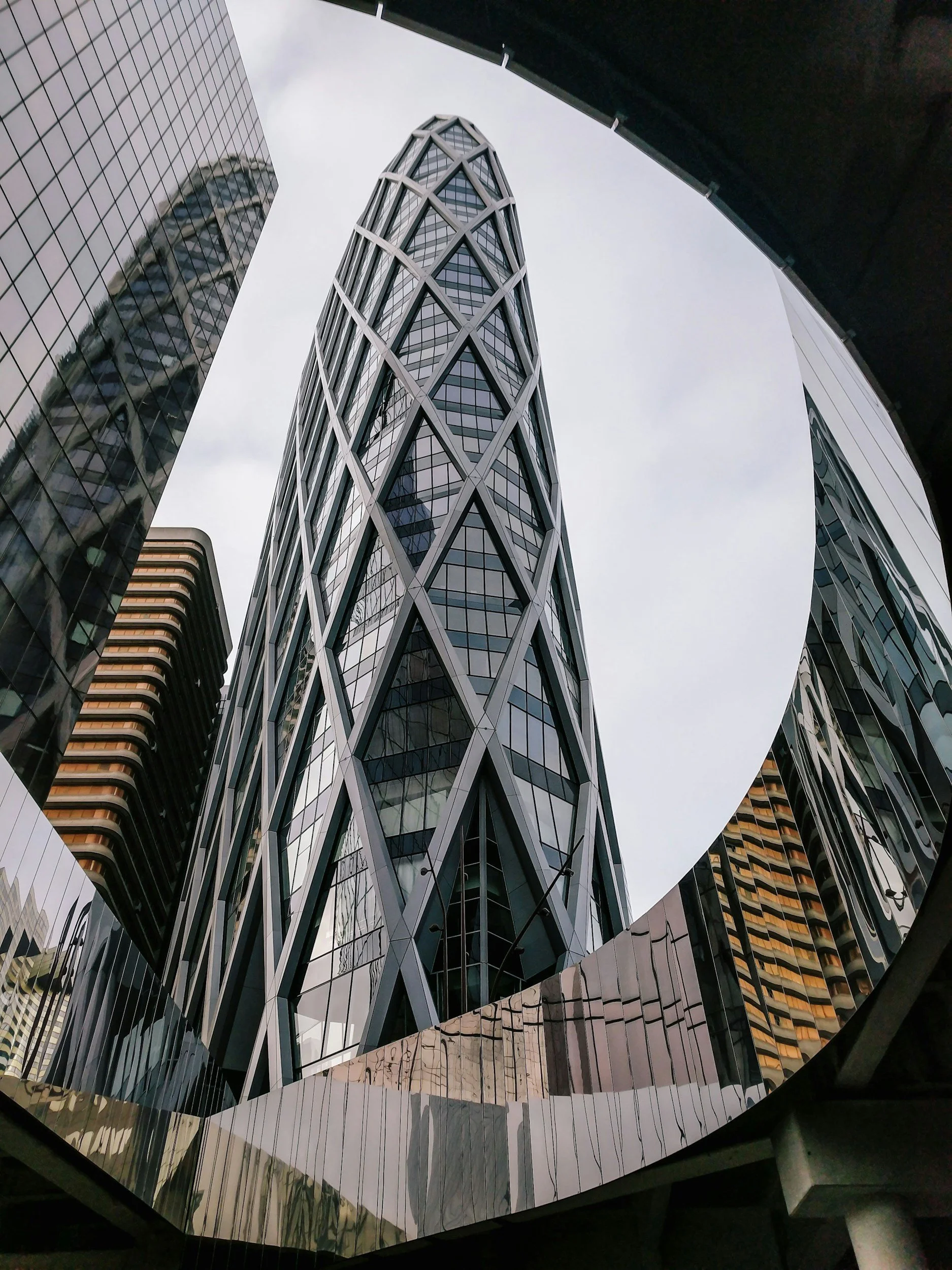 Low-angle view of modern glass skyscrapers with reflective surfaces, showing a cloudy sky.