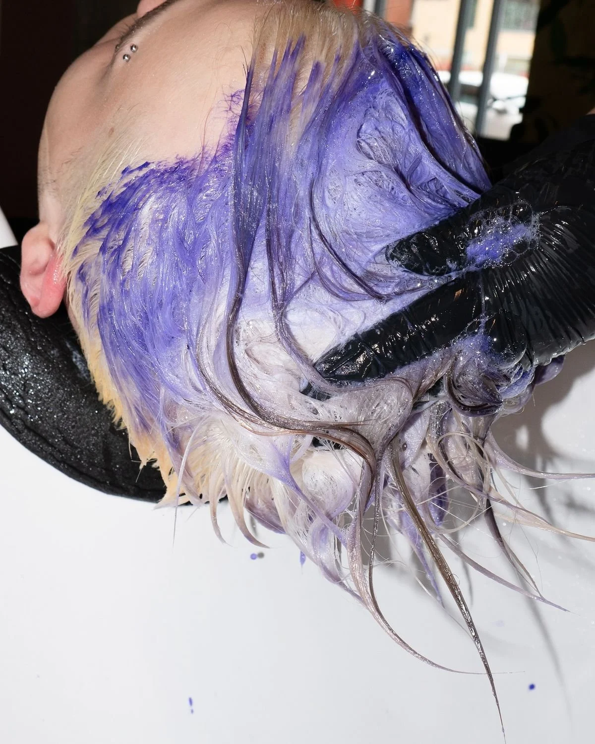 Une personne reçoit un traitement capillaire avec une mousse violette sur les cheveux, portant un bonnet noir