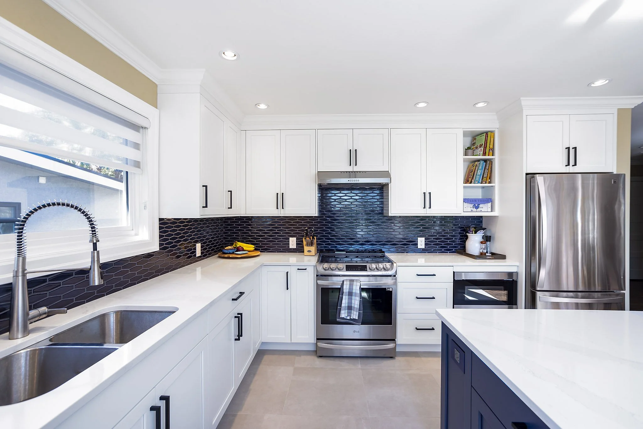 Modern kitchen with white cabinets, black hardware, stainless steel appliances, black hexagonal tile backsplash, and a large window with a white blind.