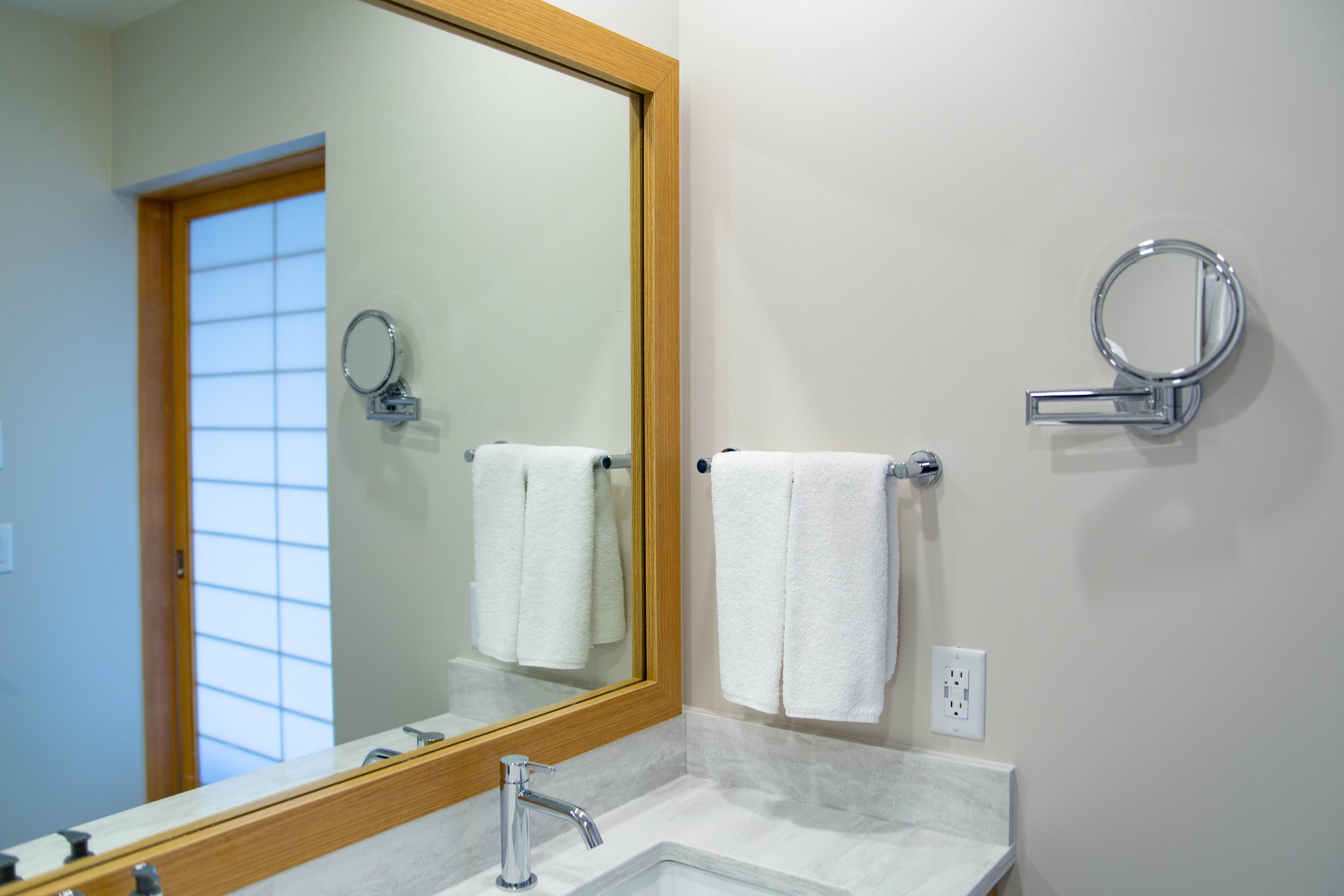 Bathroom vanity with a large mirror, white wall, towels on a towel rack, and a soap dispenser.