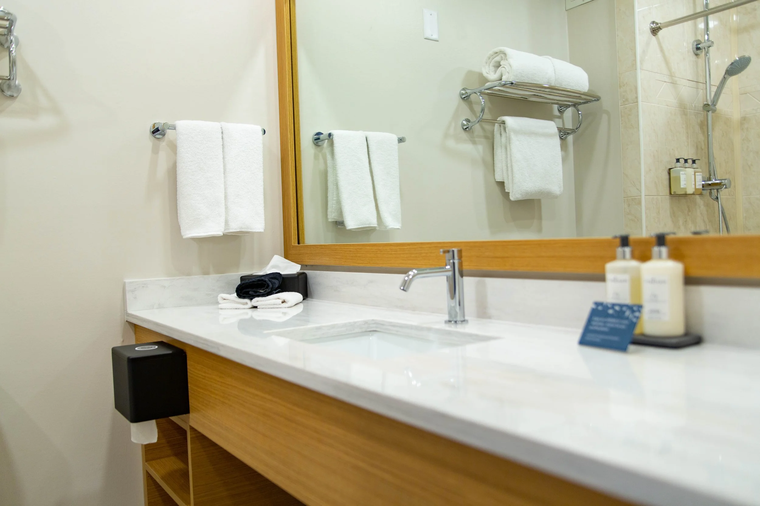 Bathroom vanity with white countertop, a sink, a mirror, and neatly folded towels hanging on a chrome rack, with toiletries on the counter.