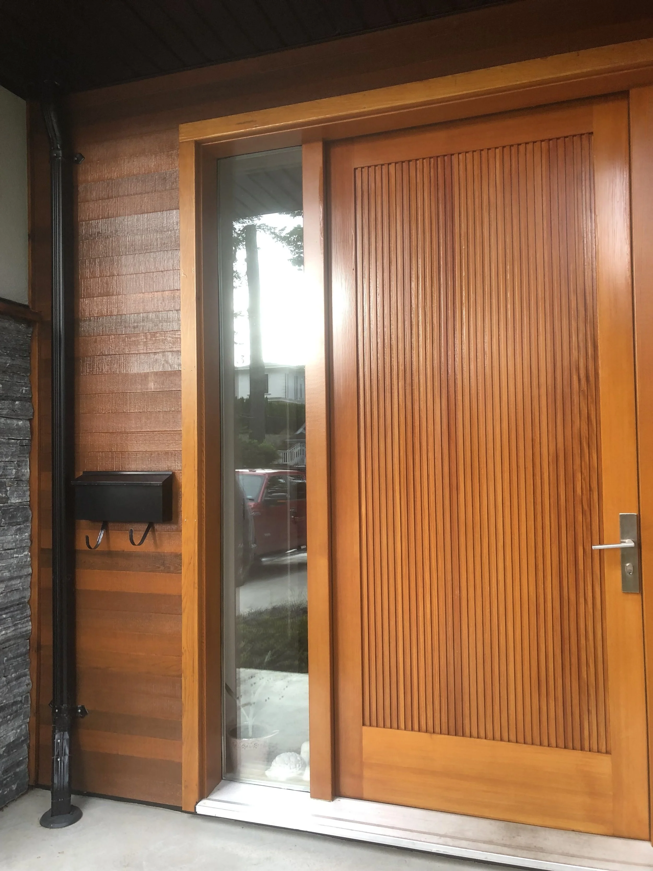 Wooden exterior door with sliding glass panel showing trees outside and a white object inside.