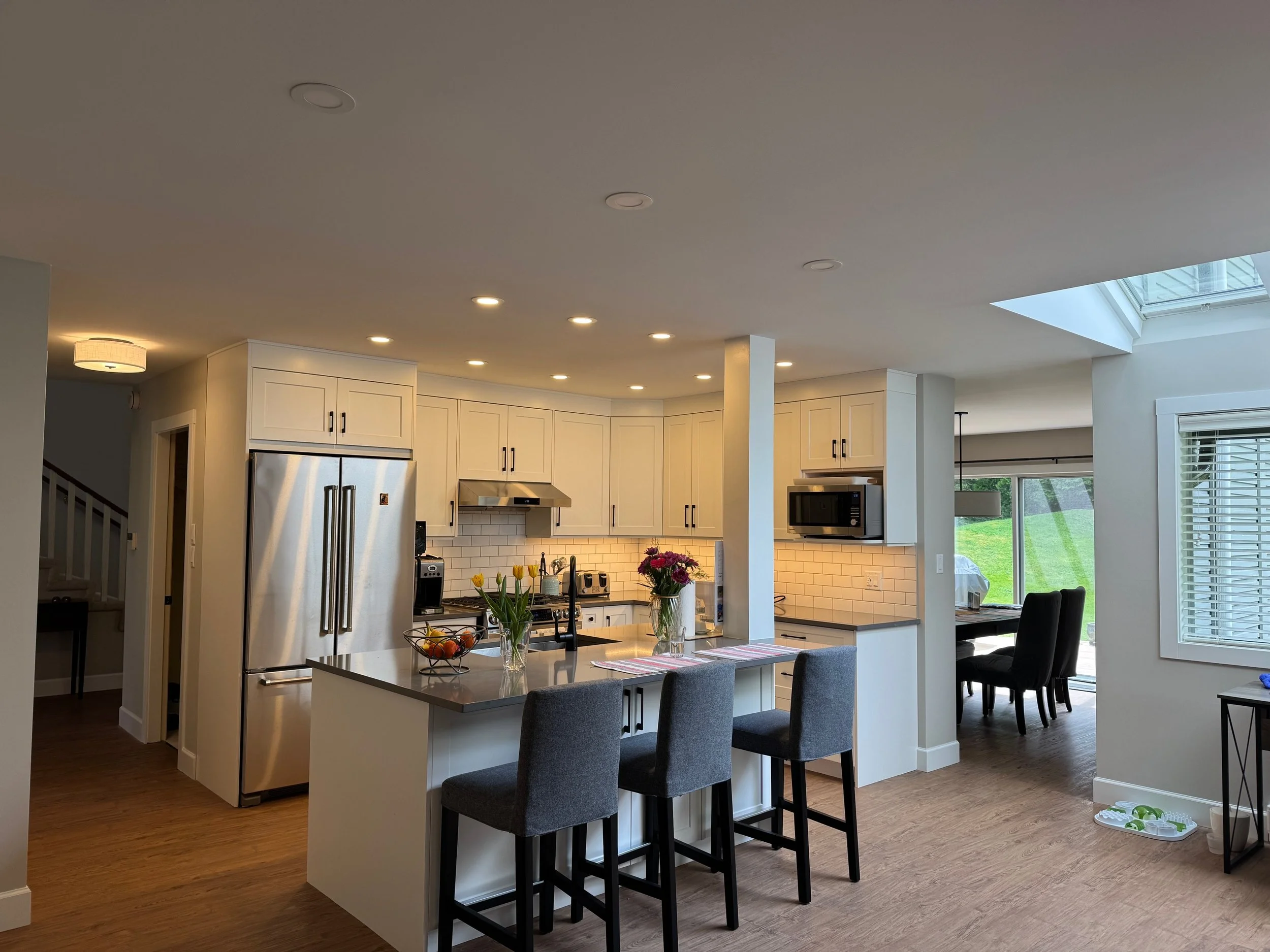 Modern kitchen with white cabinets, stainless steel appliances, a kitchen island with chairs, and a large skylight.