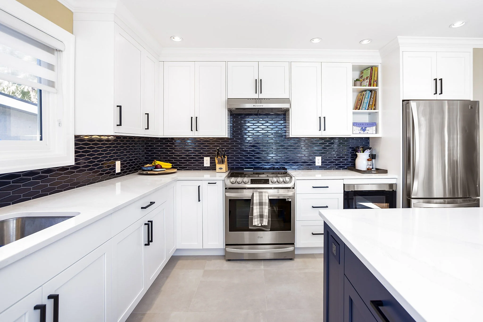 Modern kitchen with white cabinets, black handles, black hexagonal tile backsplash, stainless steel appliances, and a white countertops.