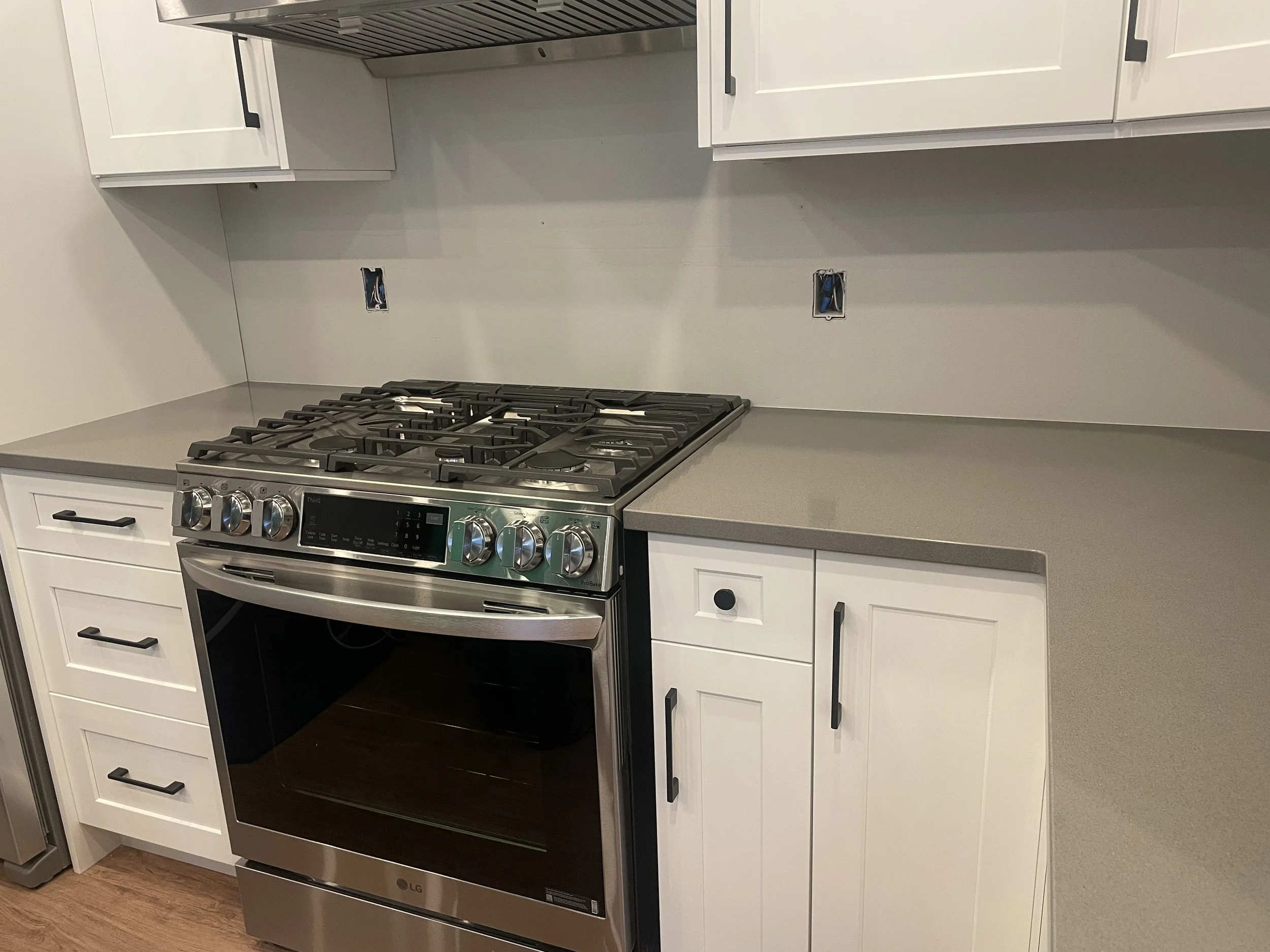 Kitchen with white cabinets and a stainless steel LG oven with a gas cooktop. There are electrical outlets and cabinets above and below the countertop.