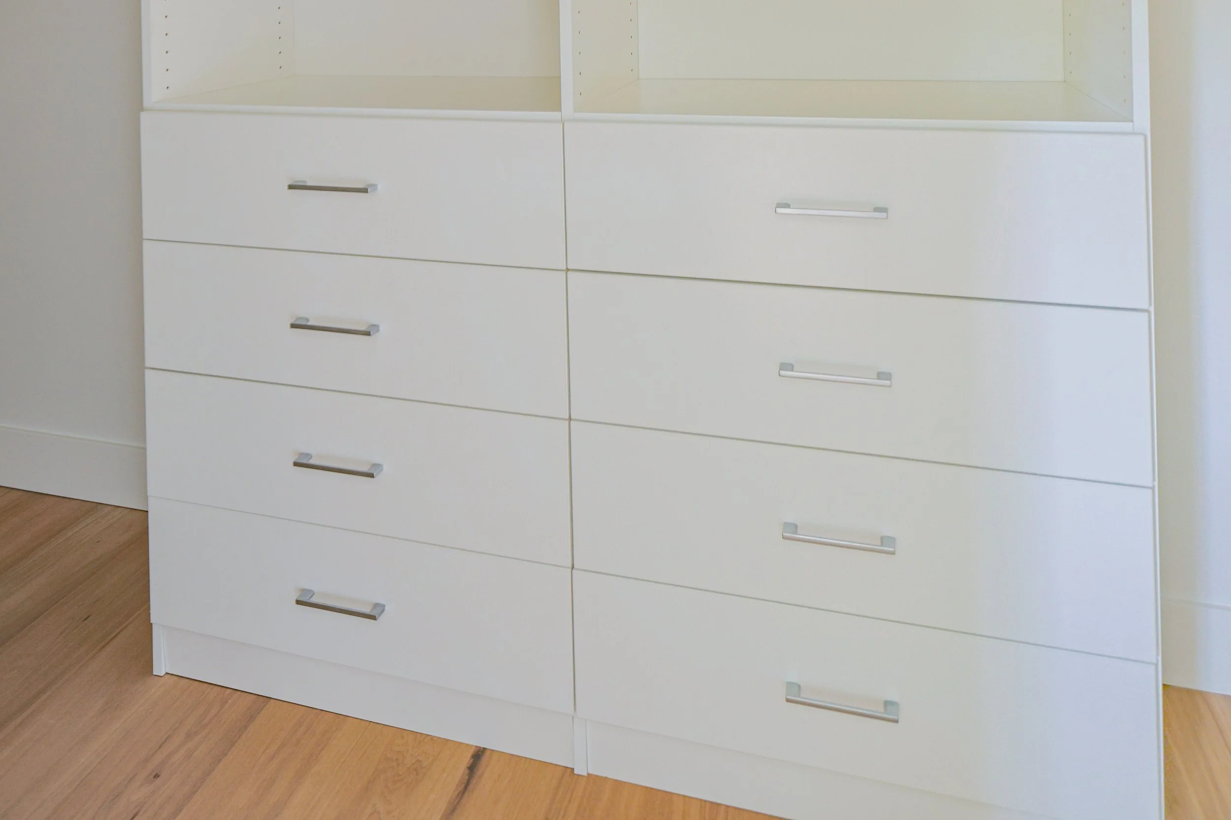 White six-drawer dresser with silver handles placed against a light-colored wall on a wooden floor.